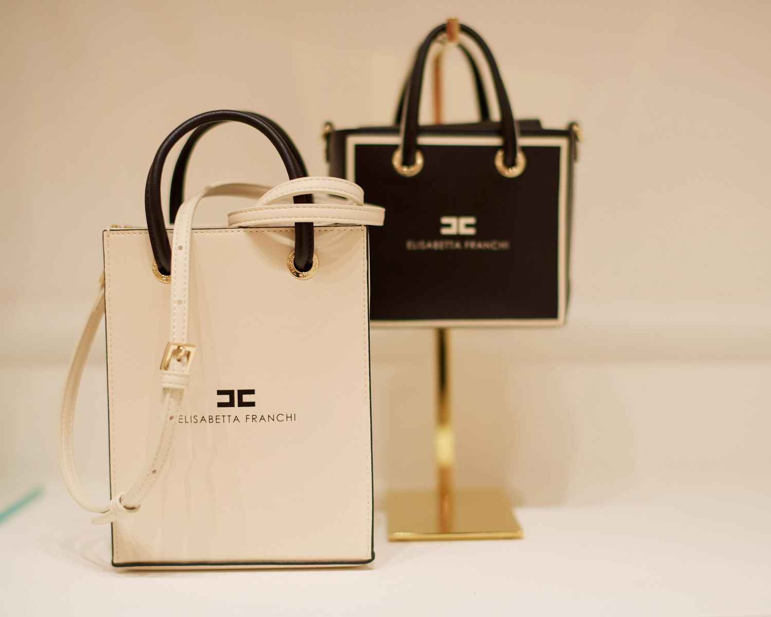 Designer handbags displayed on white pedestals in a minimalist retail setting.