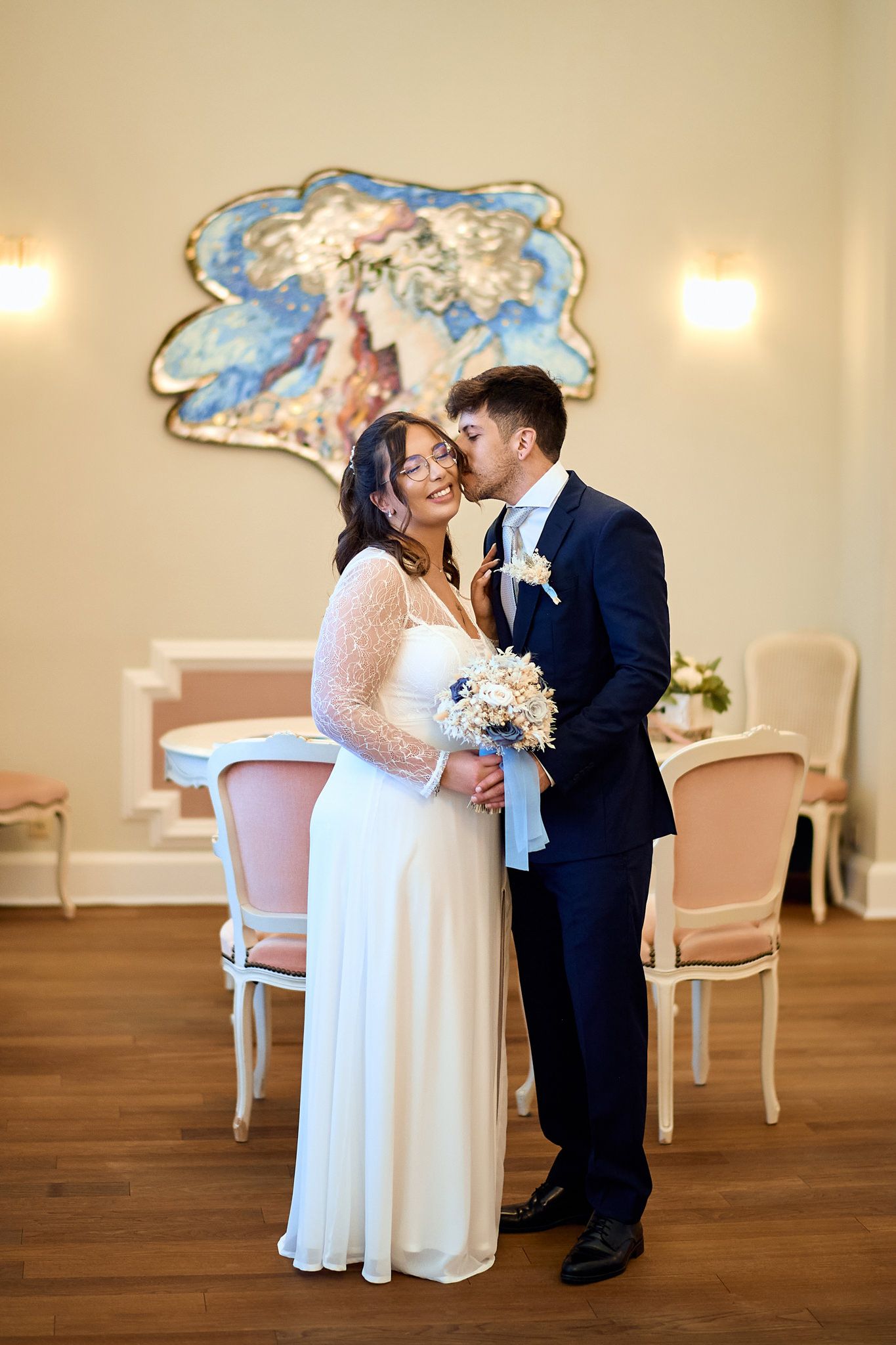 Intimate wedding moment in elegant room with ornate wall decorations and vintage chairs.