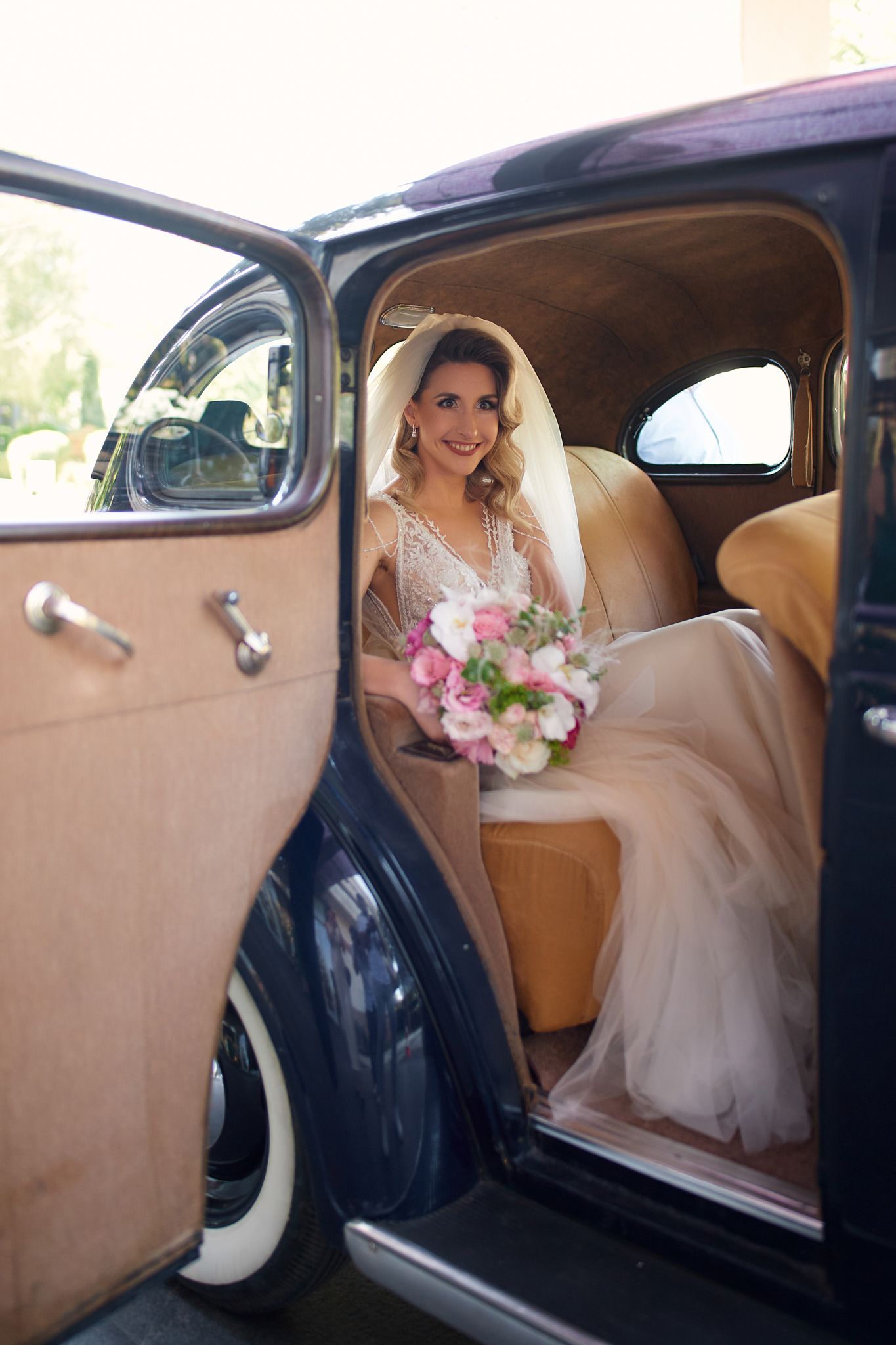 A classic vintage car interior with white wedding dress and pink bouquet details.