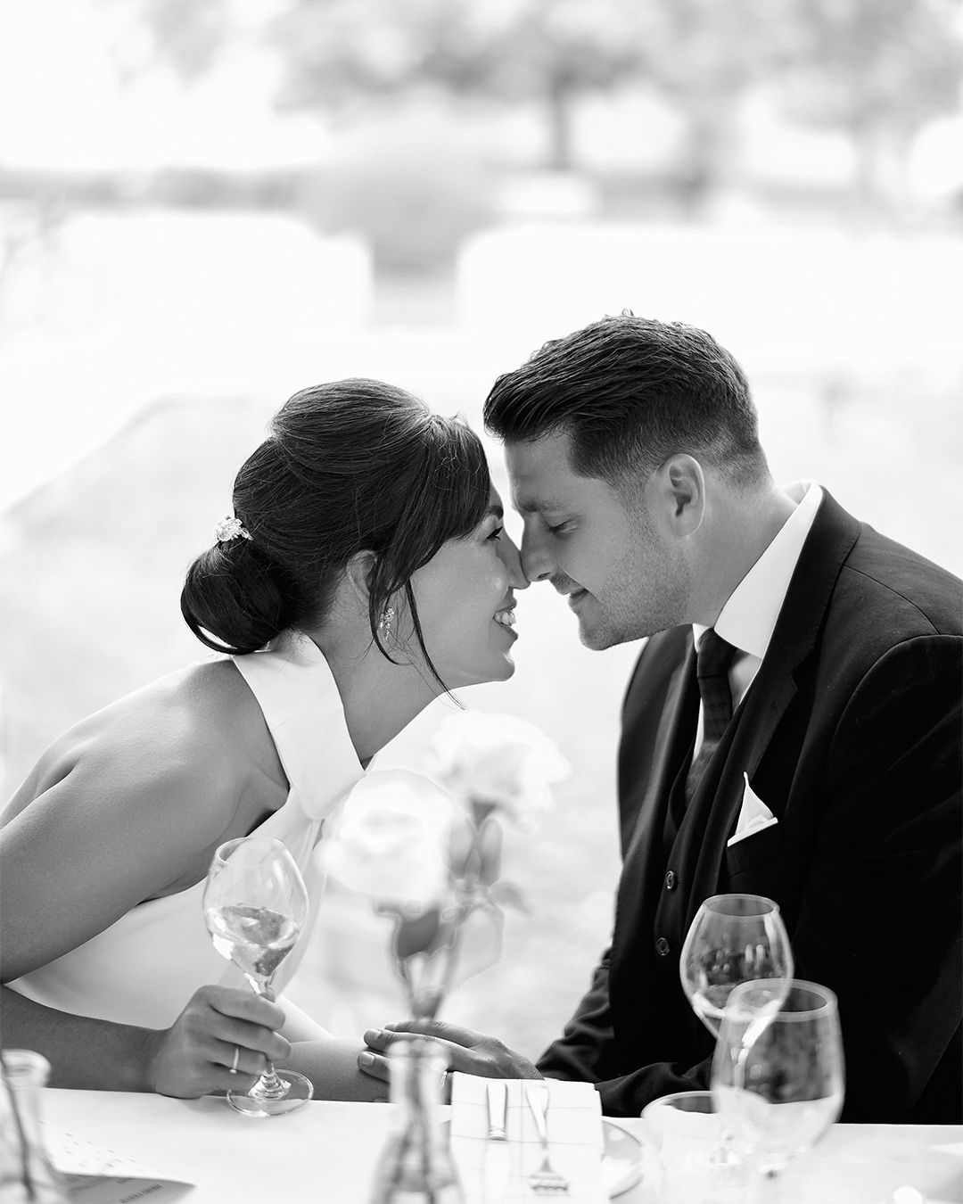 A romantic couple shares an intimate moment at a dining table with wine glasses.