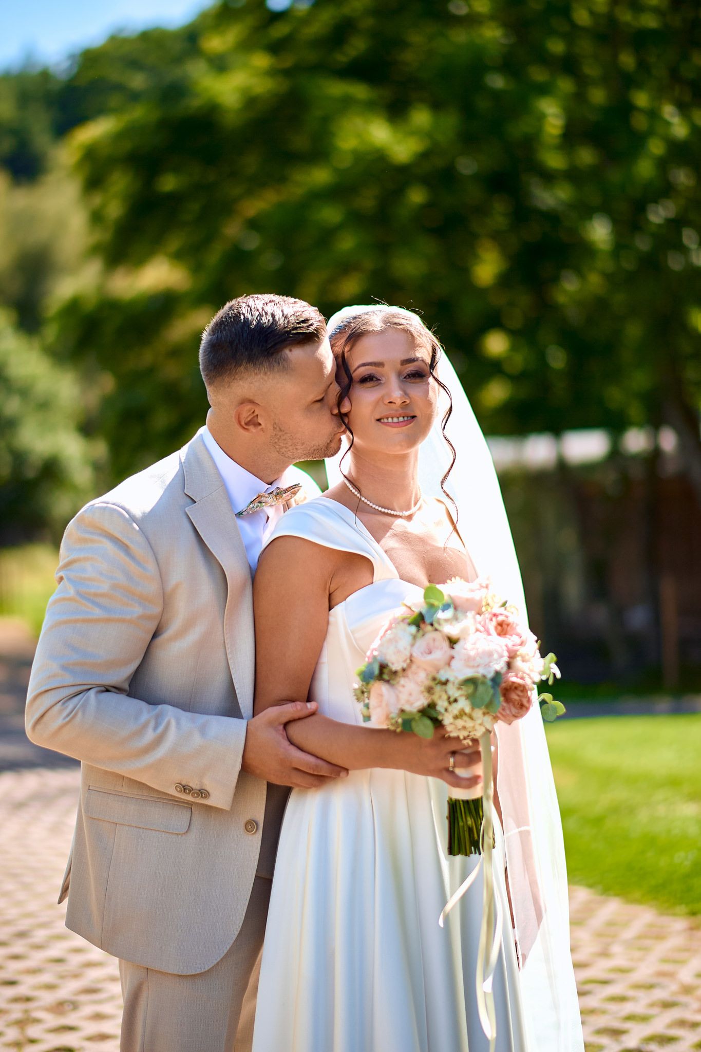 Wedding couple shares intimate moments outdoors on a sunny day with beautiful landscaping.