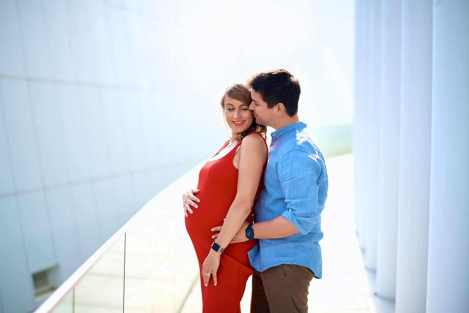Couple posing against white columns in an intimate maternity photoshoot.