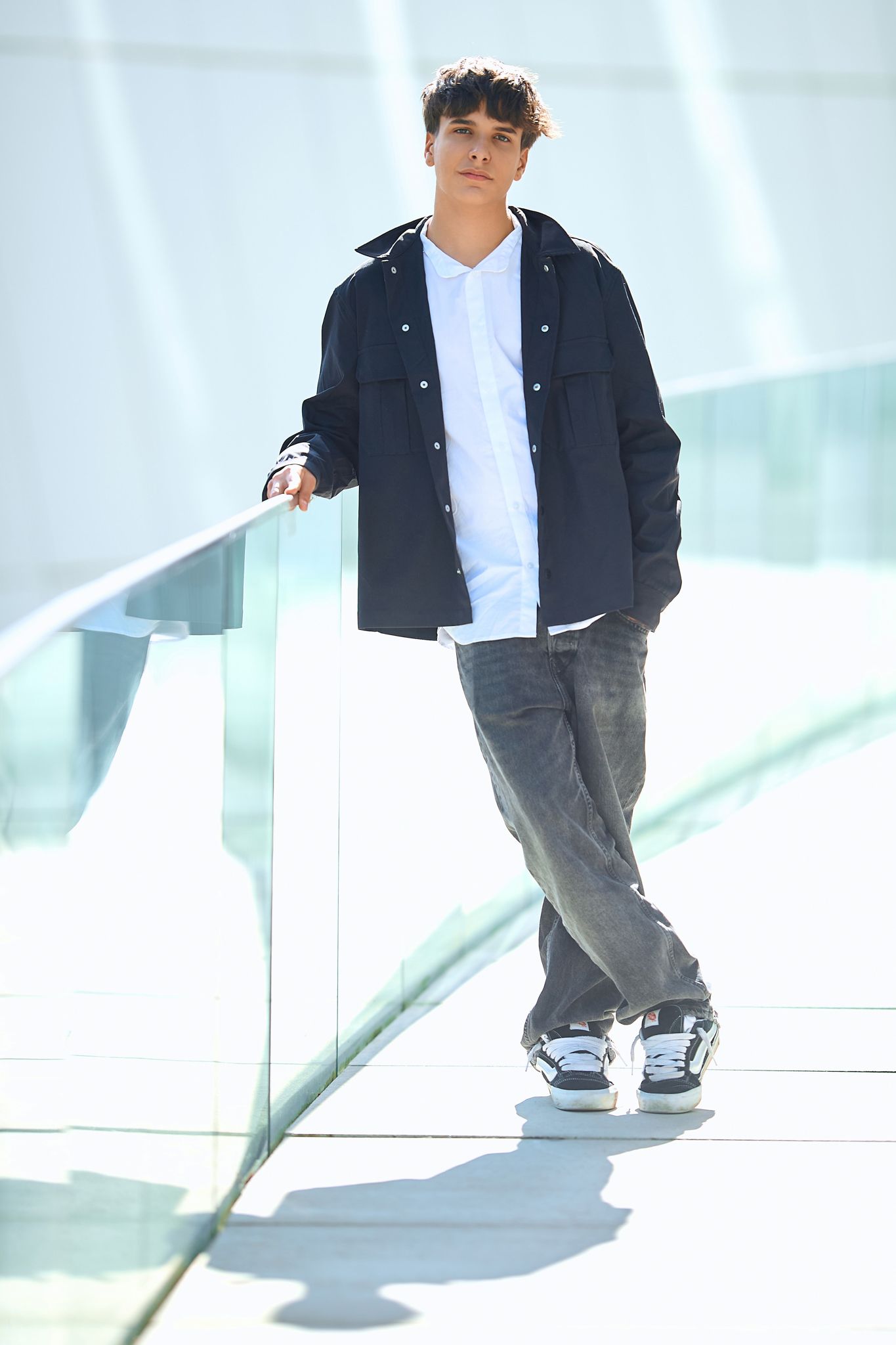 A casual fashion photo shoot featuring a black jacket and white shirt against a bright modern interior.