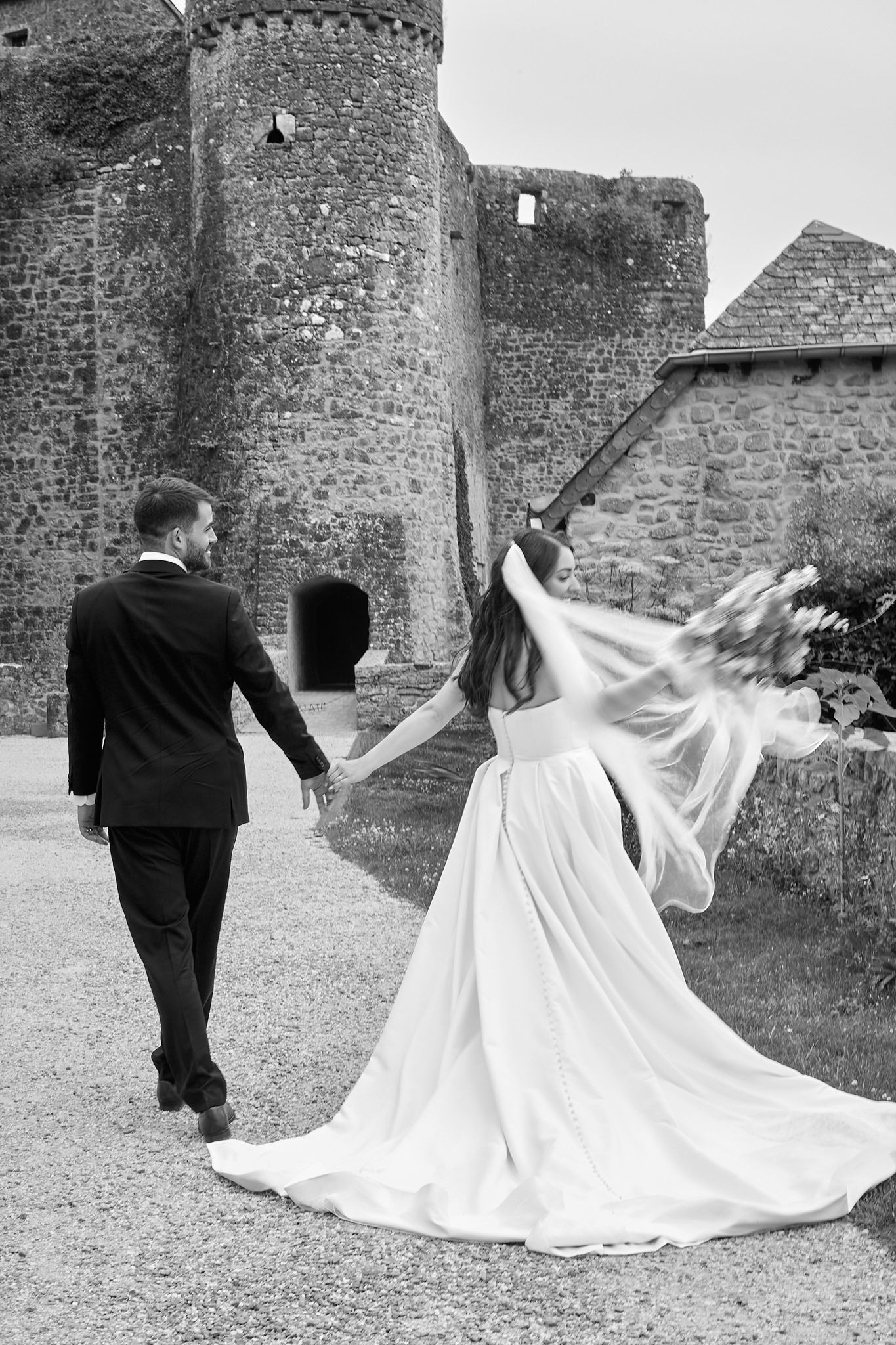 A couple walking together near historic stone castle walls with a flowing white dress train.