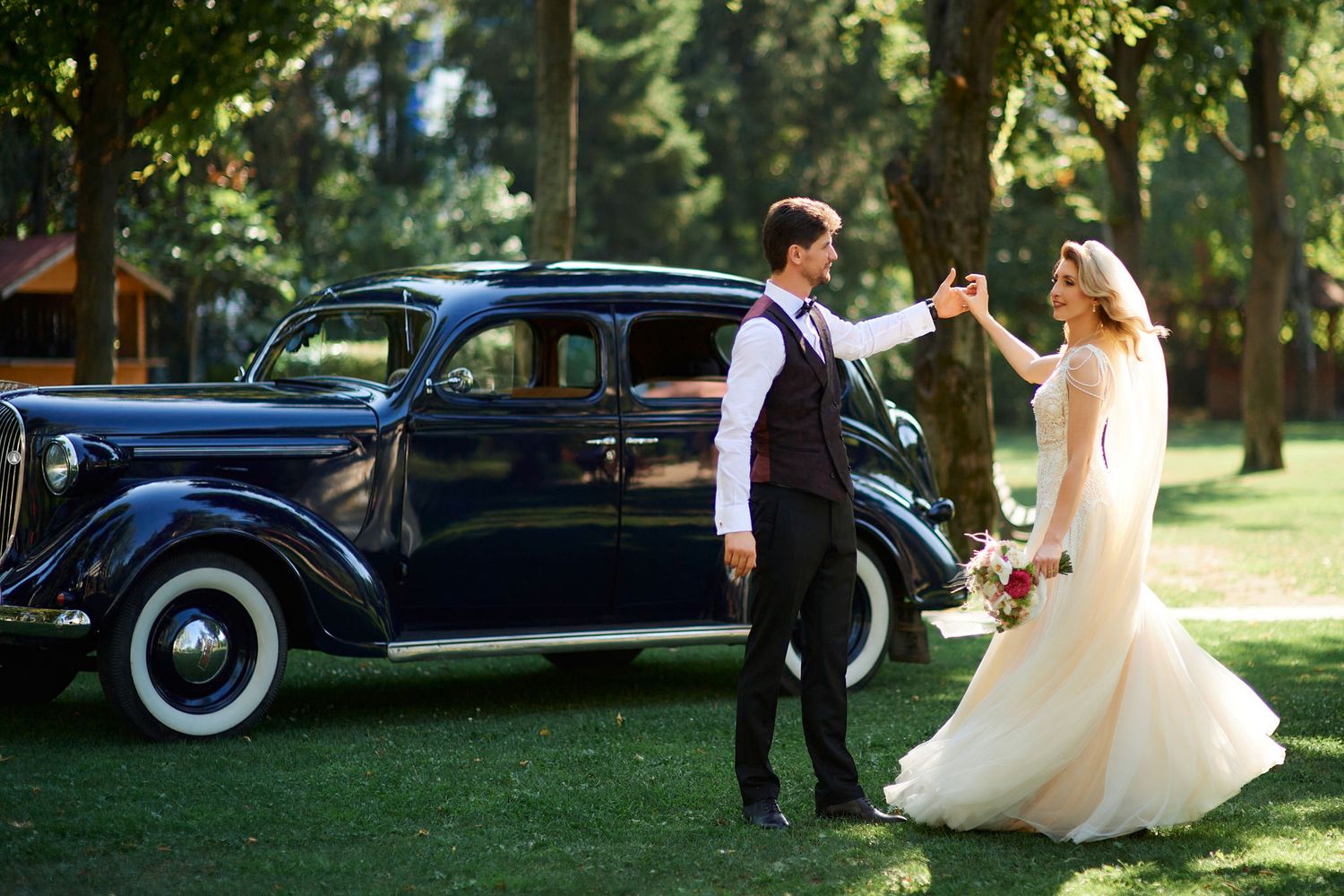 A vintage navy blue car parked on grass during a wedding photoshoot.