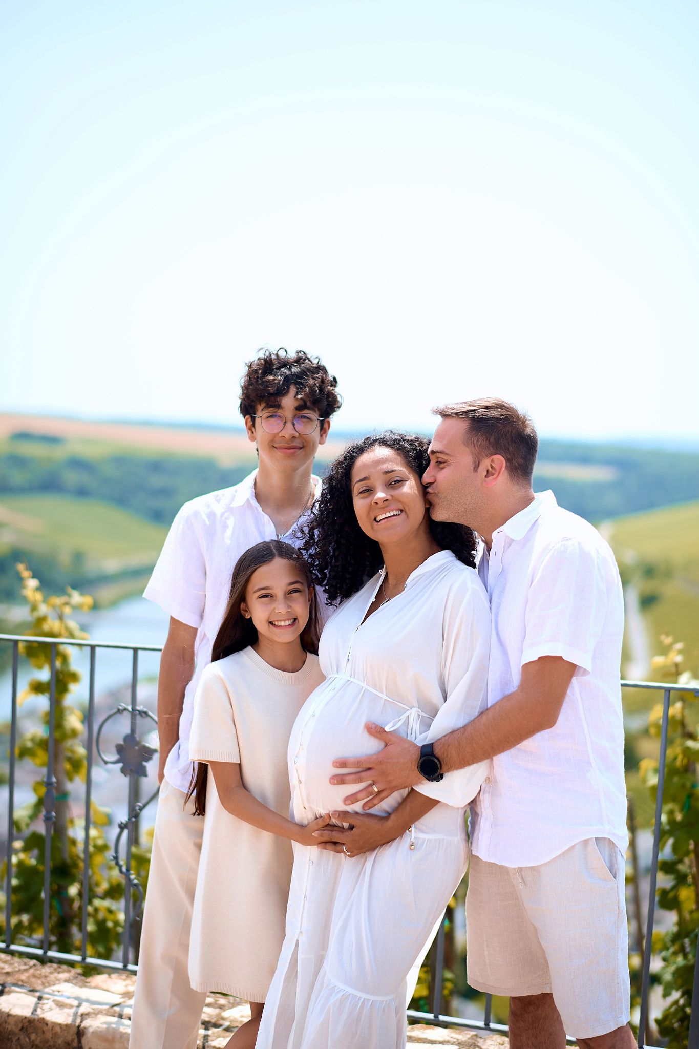 Family wearing white outfits poses together outdoors against scenic mountain backdrop.