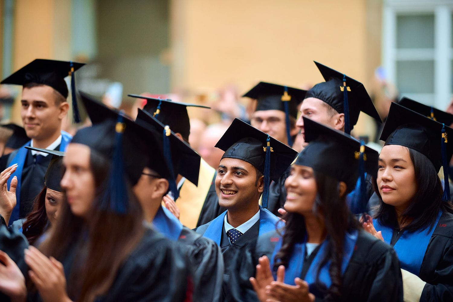 Graduates in black caps and gowns with blue stoles celebrate during commencement ceremony.