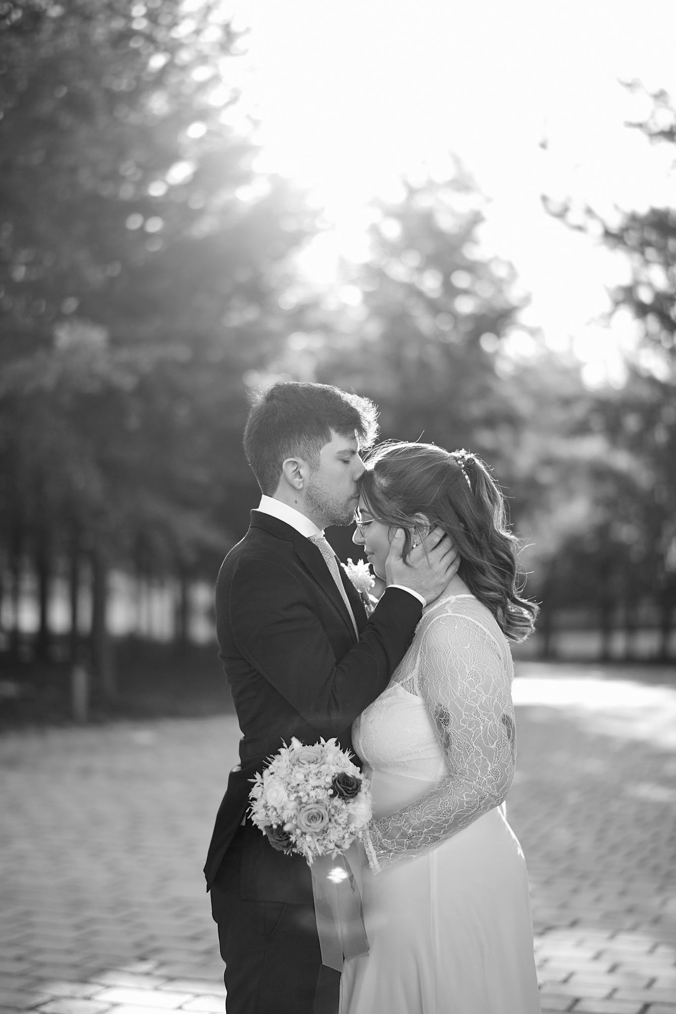A romantic black and white wedding photo captured in soft sunlight with a bouquet.