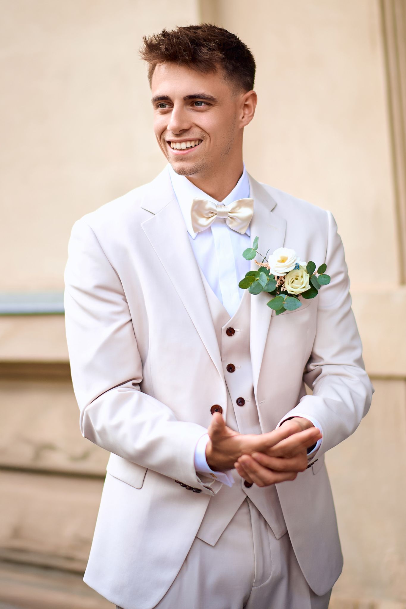 Groom in white tuxedo with boutonniere adjusts his bowtie in sequence.