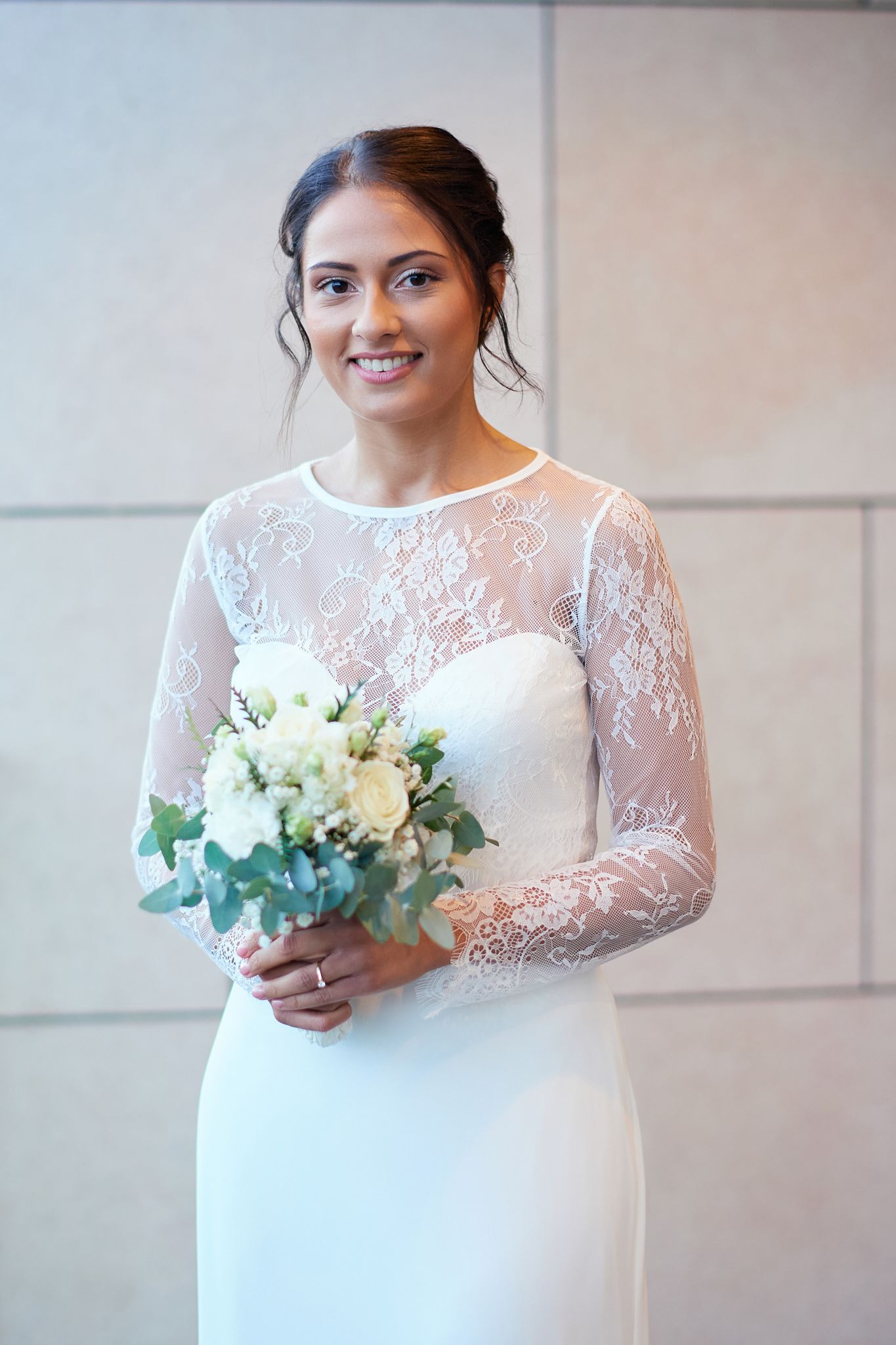 Bride wearing long sleeve lace wedding dress holds white and green bouquet.