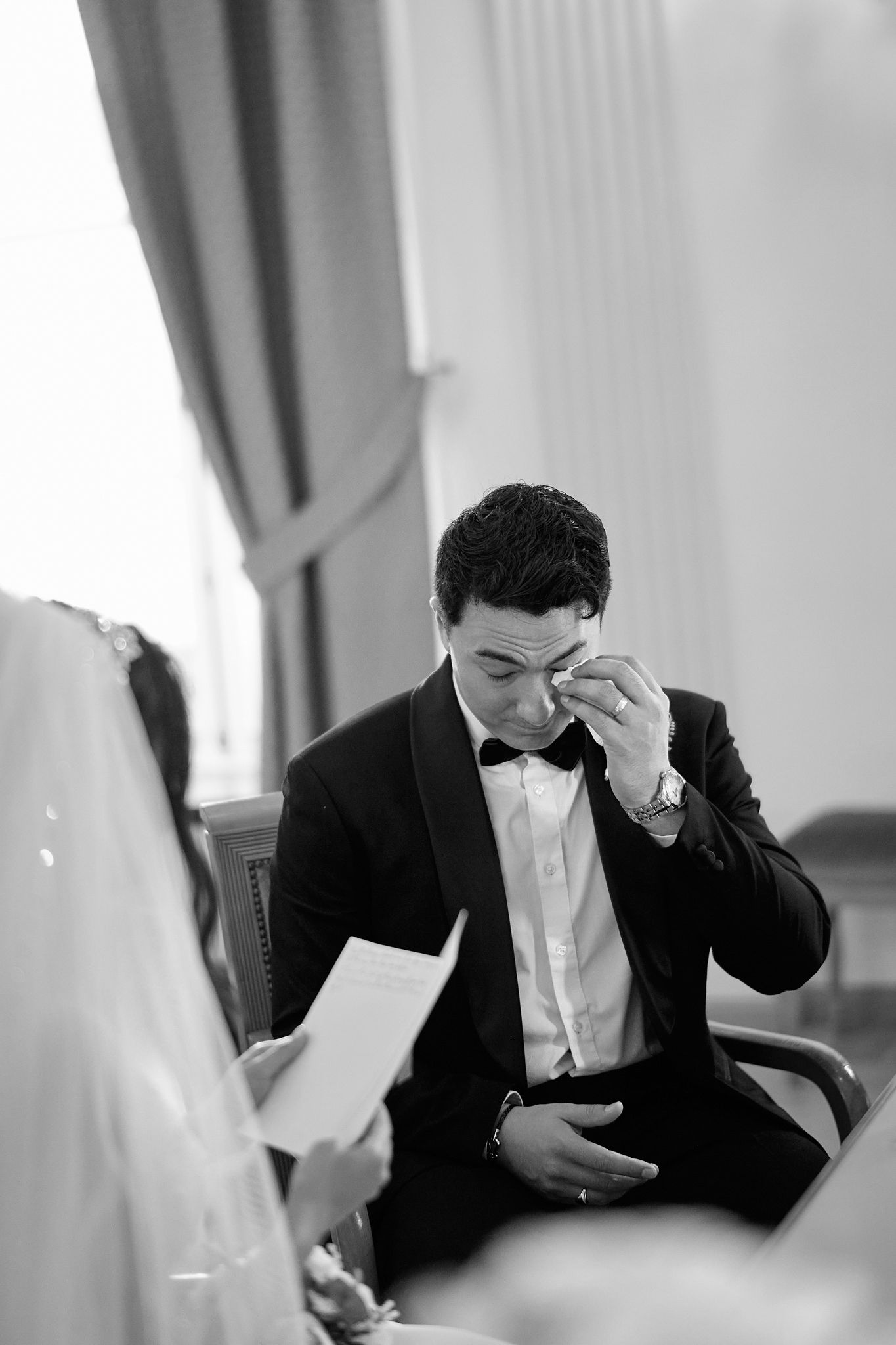 Emotional groom wipes tears during wedding ceremony in formal attire.