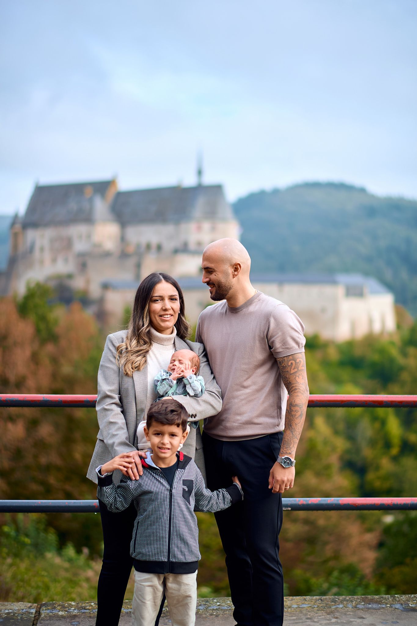 Family portrait taken outdoors with historic castle visible in background on cloudy day.