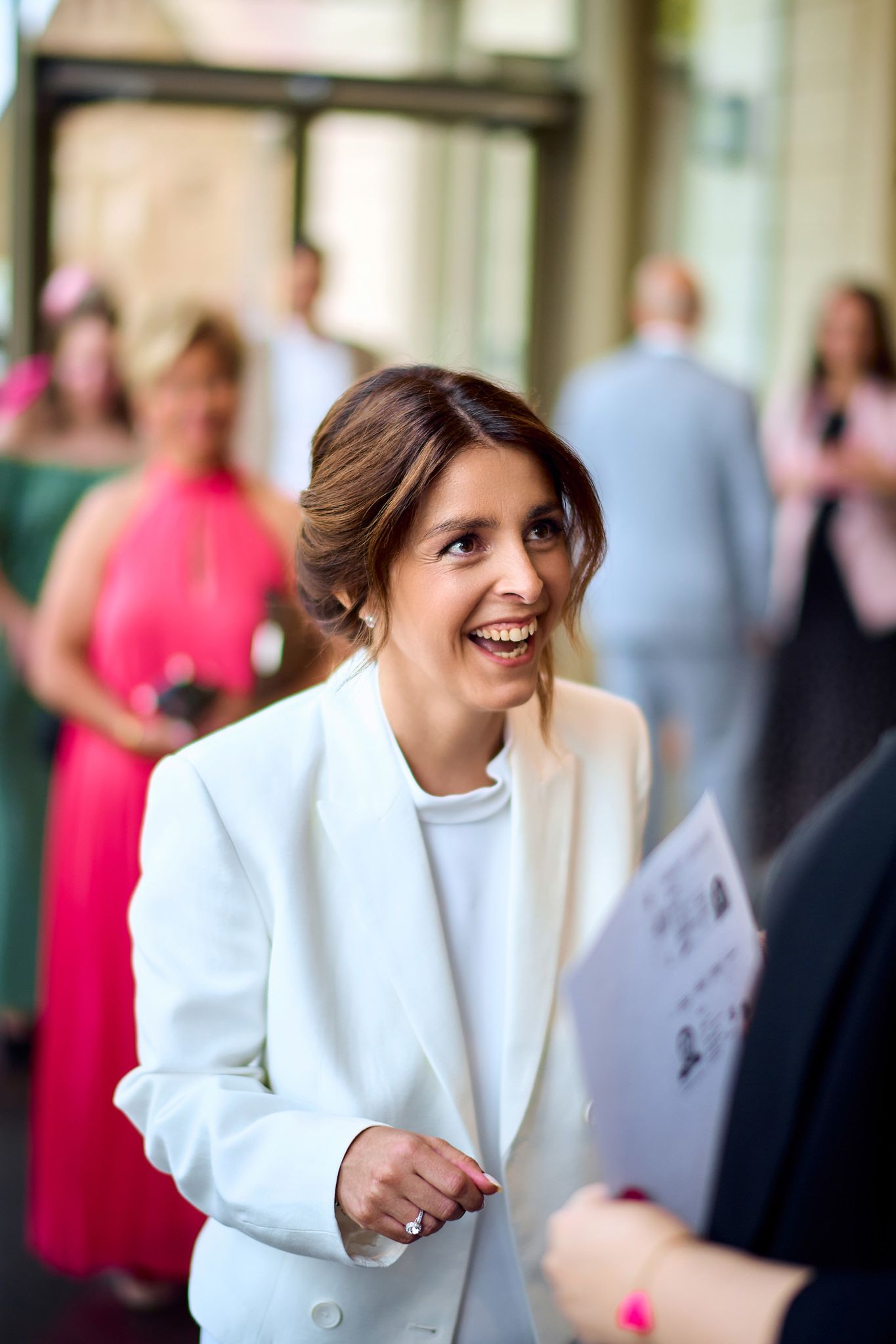 A person in a white blazer smiles and laughs during an outdoor event.