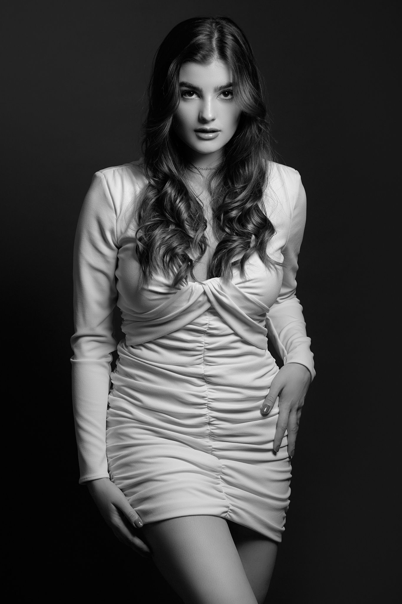 Fashion portrait of a model in a white ruched dress against a dark background.