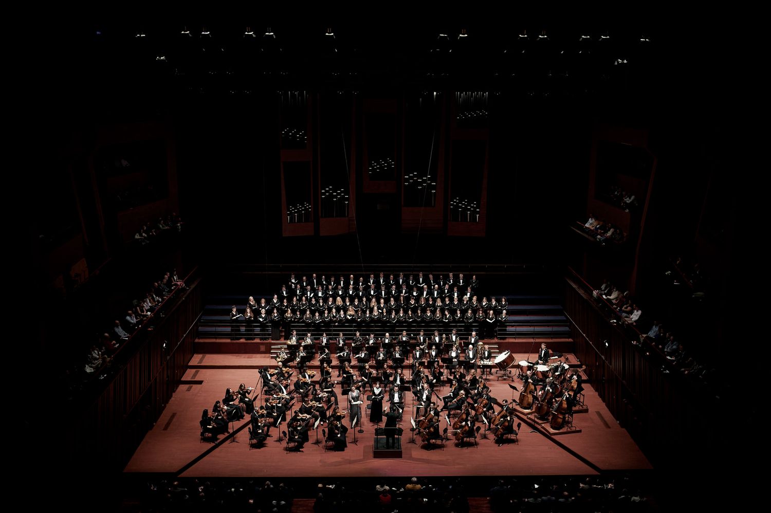 Symphony orchestra performs on dimly lit concert hall stage.