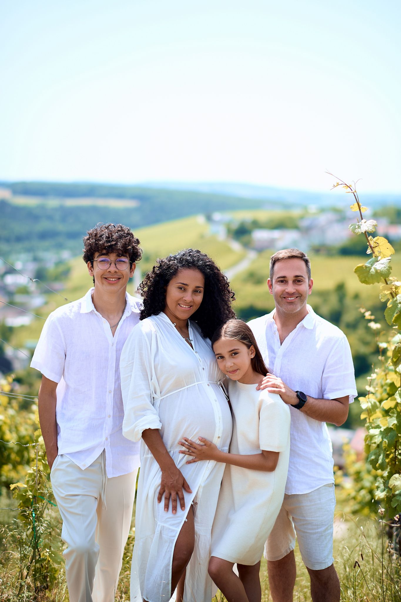 Family group in coordinated white outfits poses together on hilltop with scenic view.