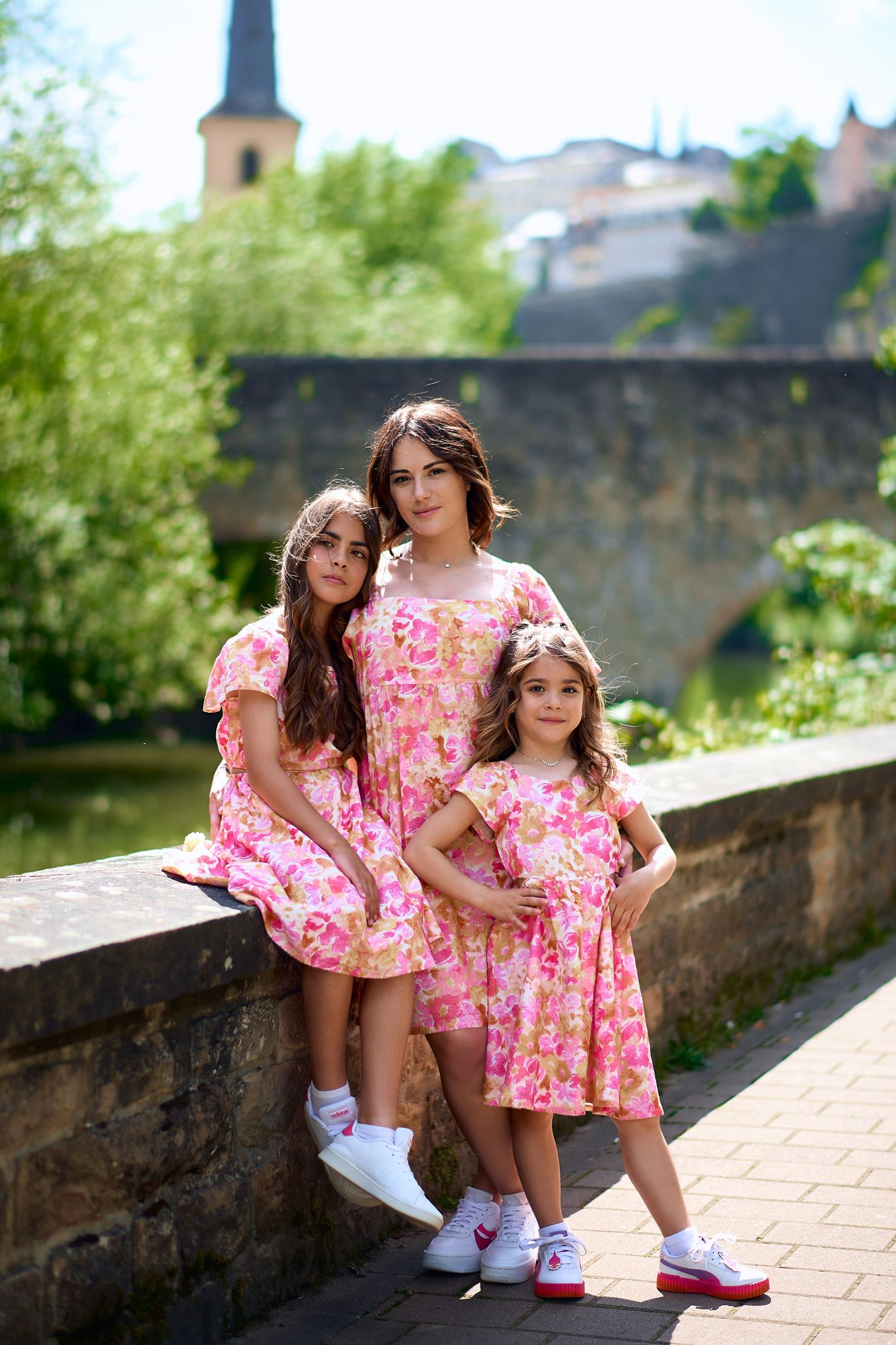 Children in matching pink dresses playing and posing on stone pathway.