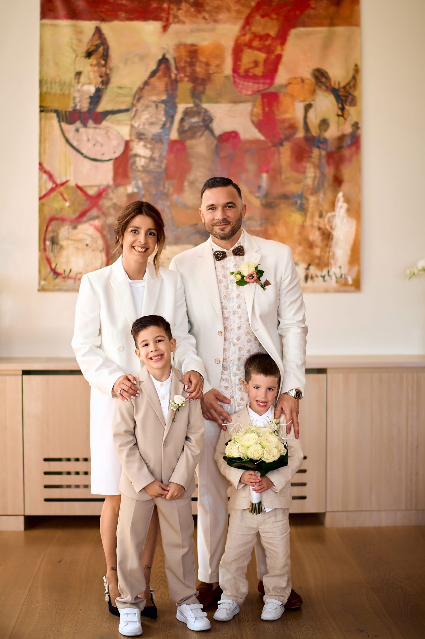Wedding party members in light gray suits pose together against colorful abstract artwork in an elegant venue.