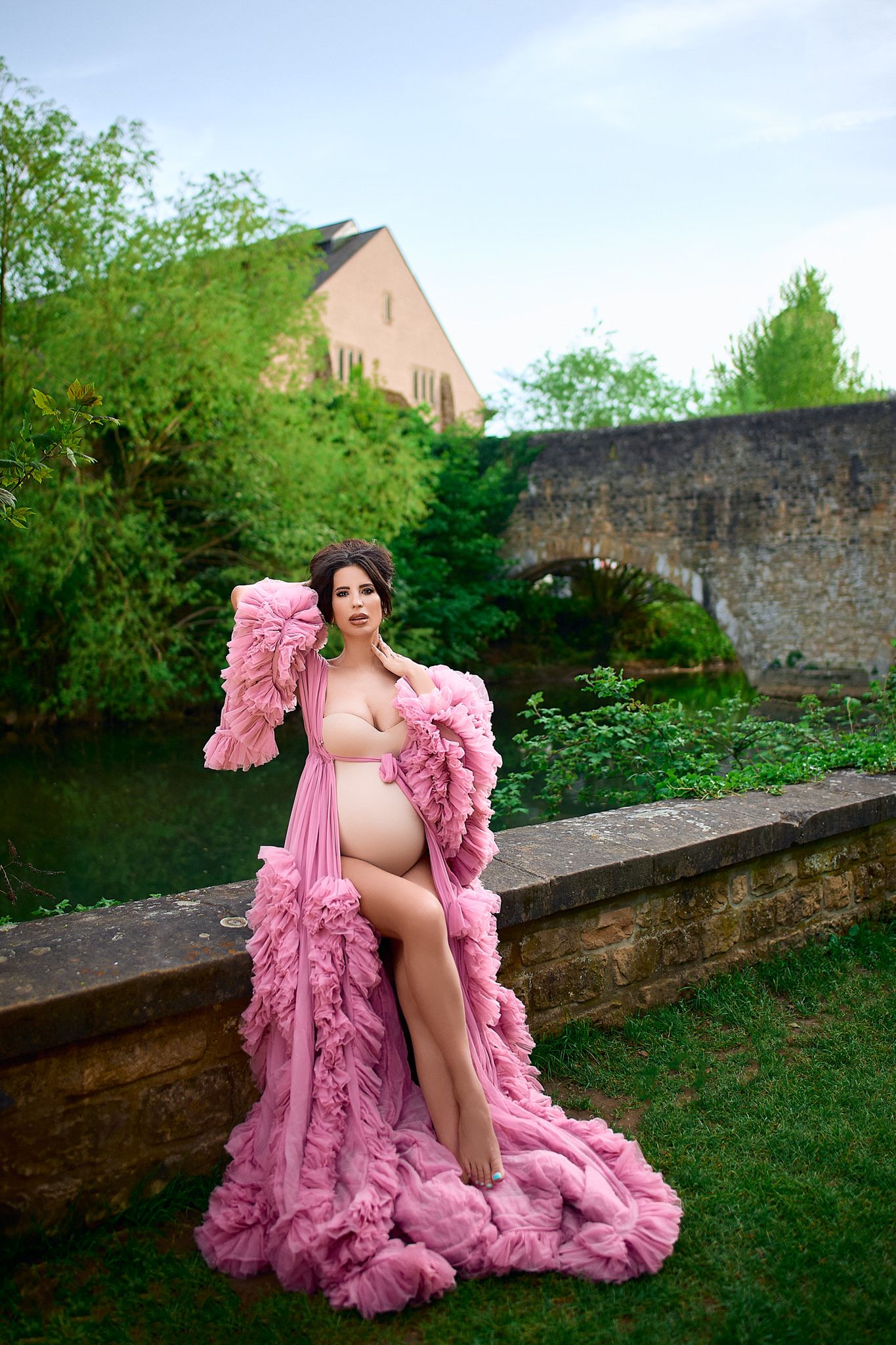 Pink ruffled tulle gown draped elegantly against stone wall backdrop in outdoor garden setting.