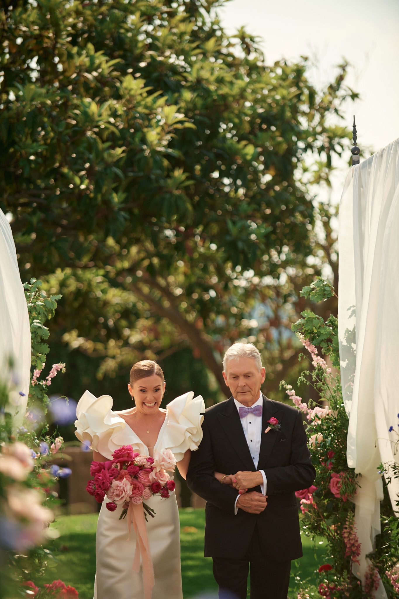 Wedding couple shares a romantic moment under floral arches in an outdoor garden ceremony.