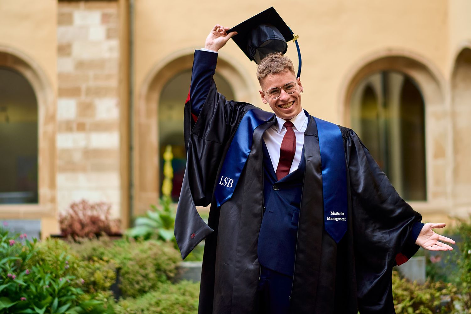 Graduates celebrate with hugs and smiles in front of stone archways.