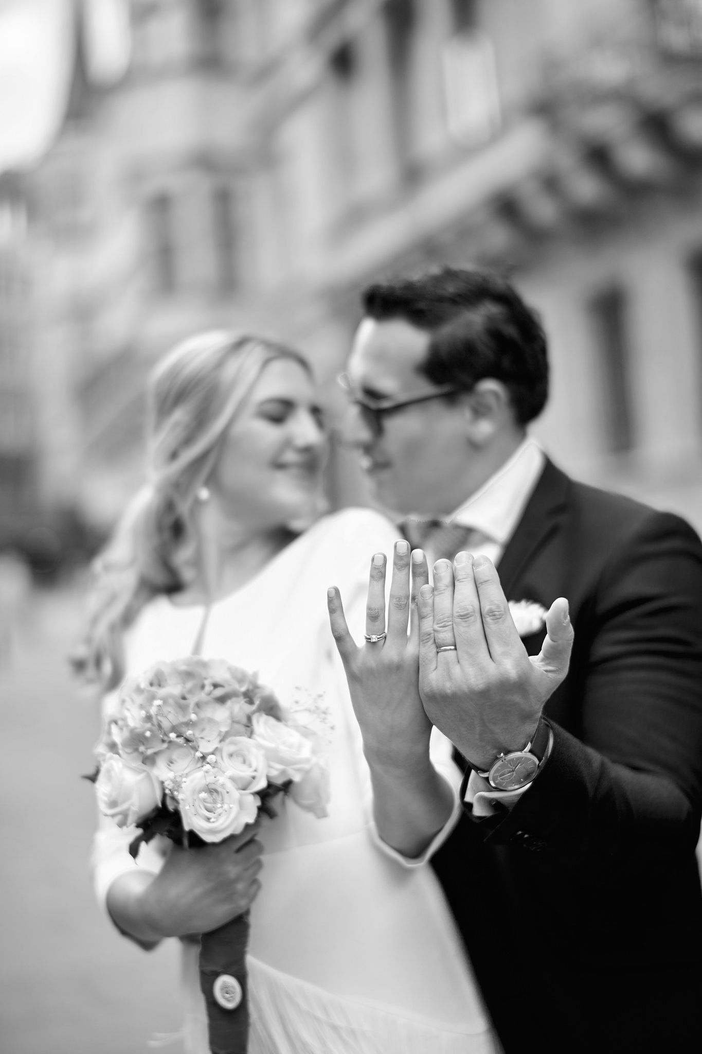 A couple in wedding attire shows off their rings in a creative black and white photo.