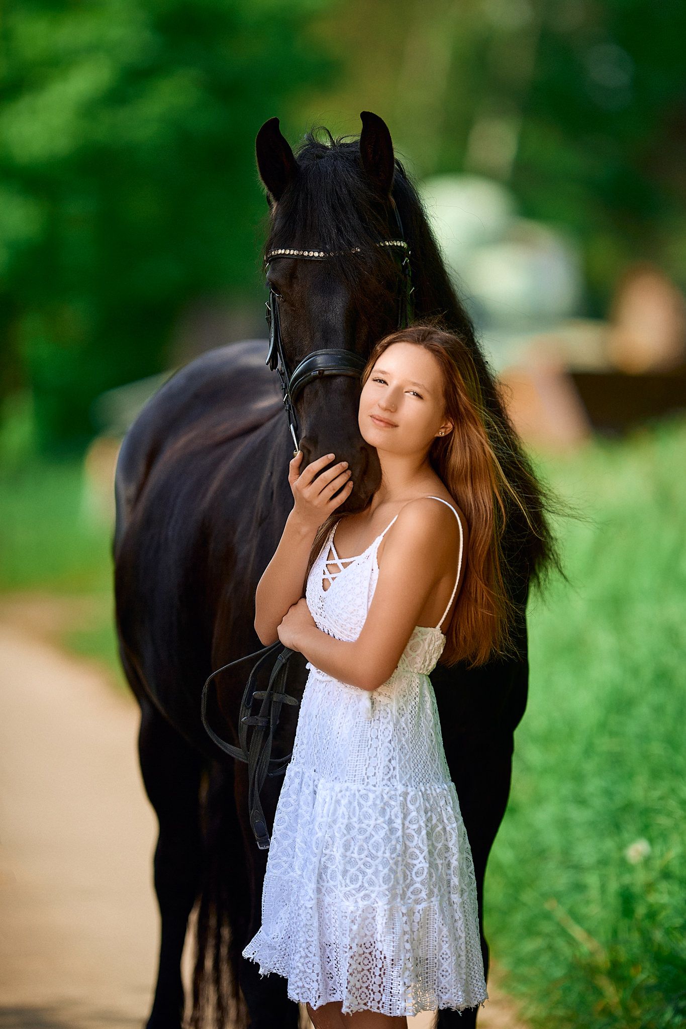 Young person in white lace dress standing beside black horse in green outdoor setting.