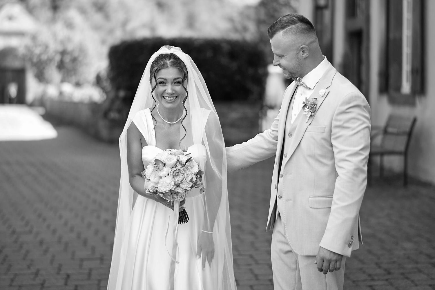 A couple in white wedding attire shares an intimate moment outdoors.
