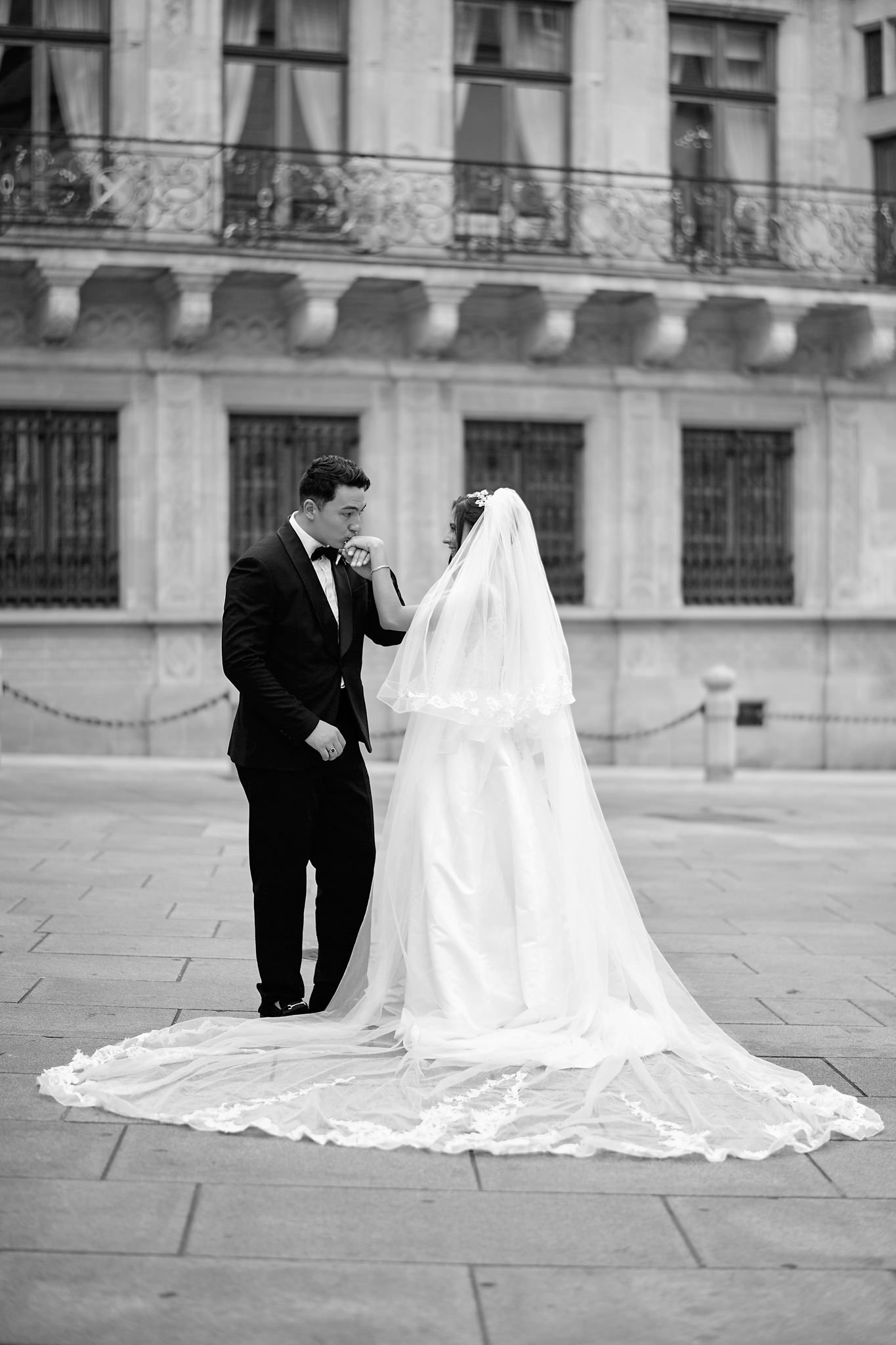 Dramatic black and white wedding portraits with flowing veil against historic building backdrop.