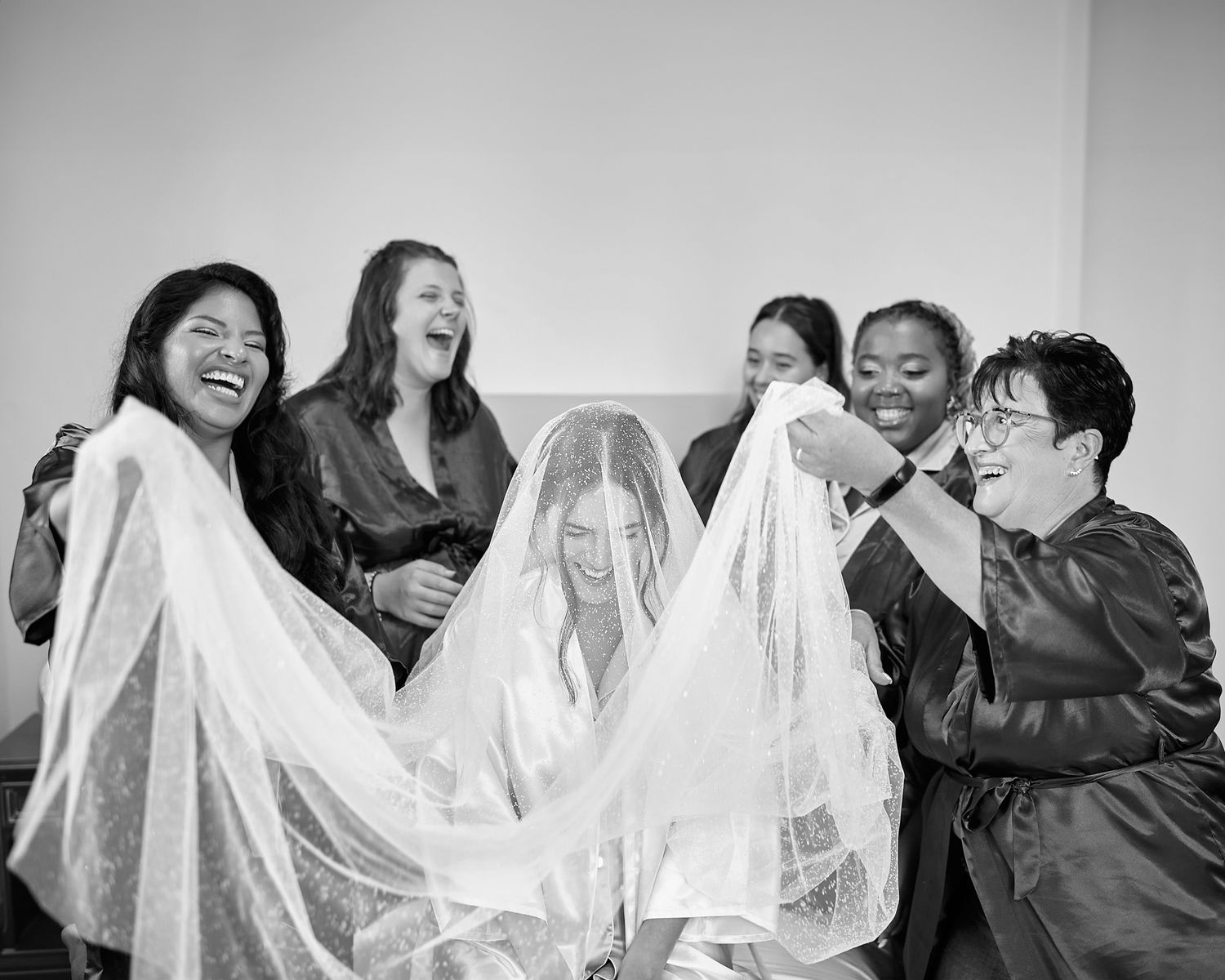 Joyful candid moment with bridesmaids playing with wedding veil.