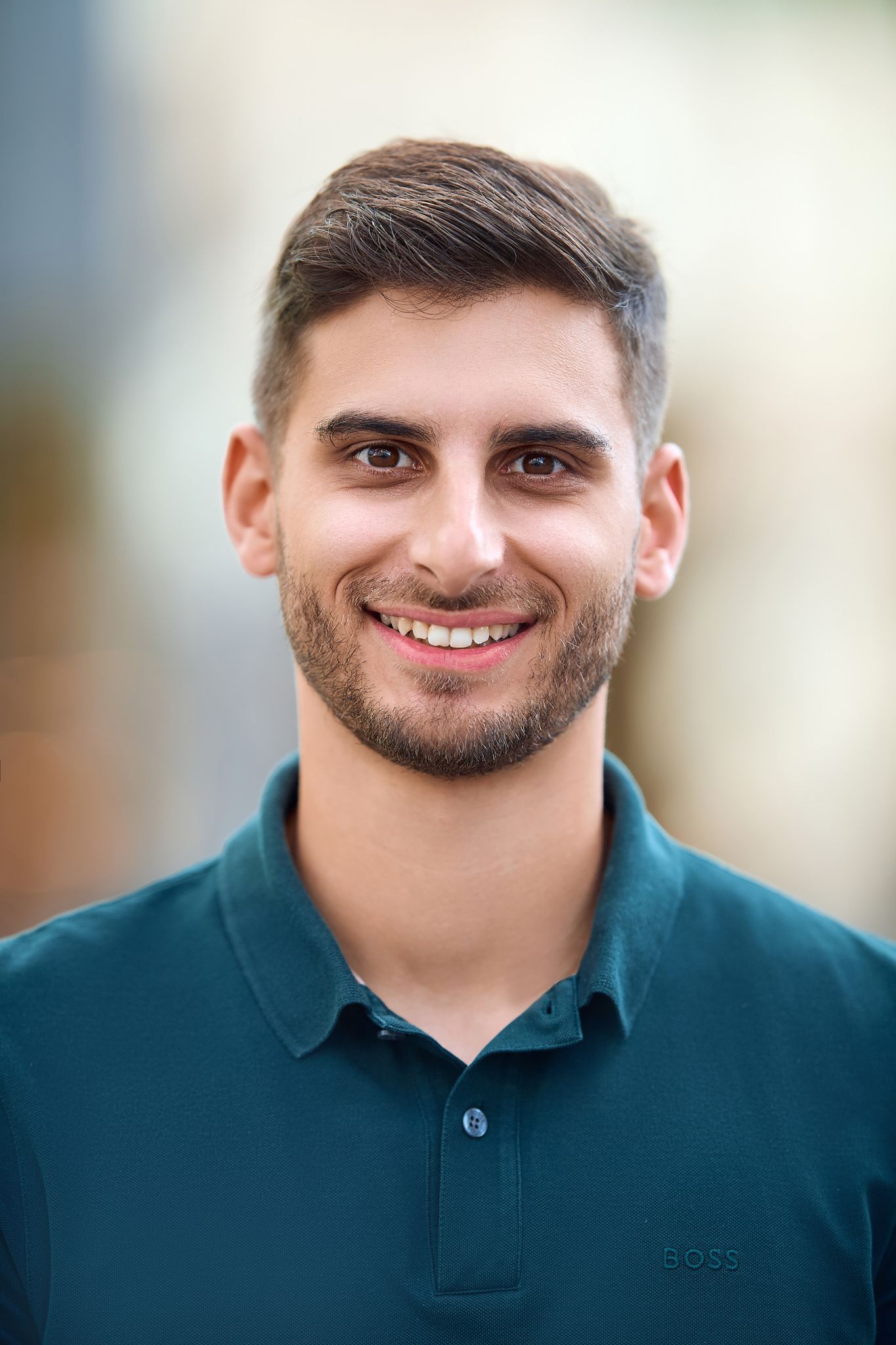 Professional headshot in teal polo shirt against soft focus background.