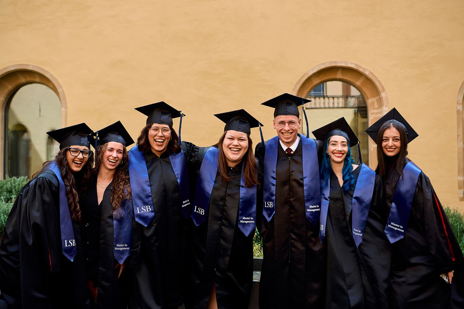 Group of graduates in blue caps and gowns posing together outdoors.