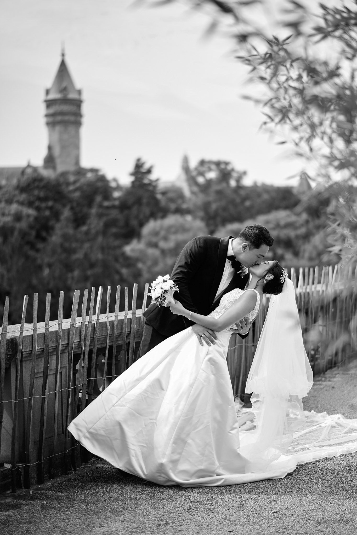 Black and white wedding photos showing romantic poses along a fence with a church spire in background.