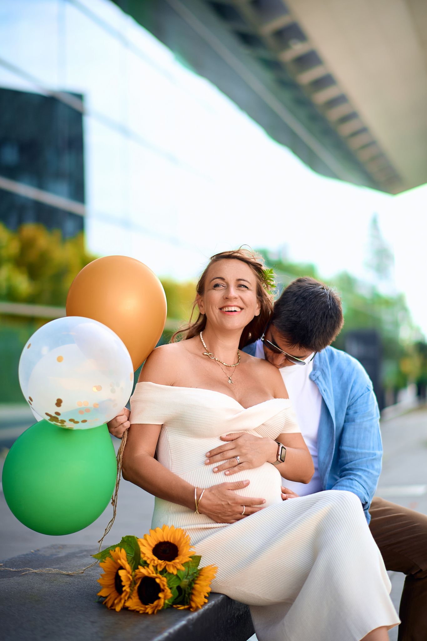Maternity photoshoot with white and green balloons and sunflowers against an outdoor backdrop.