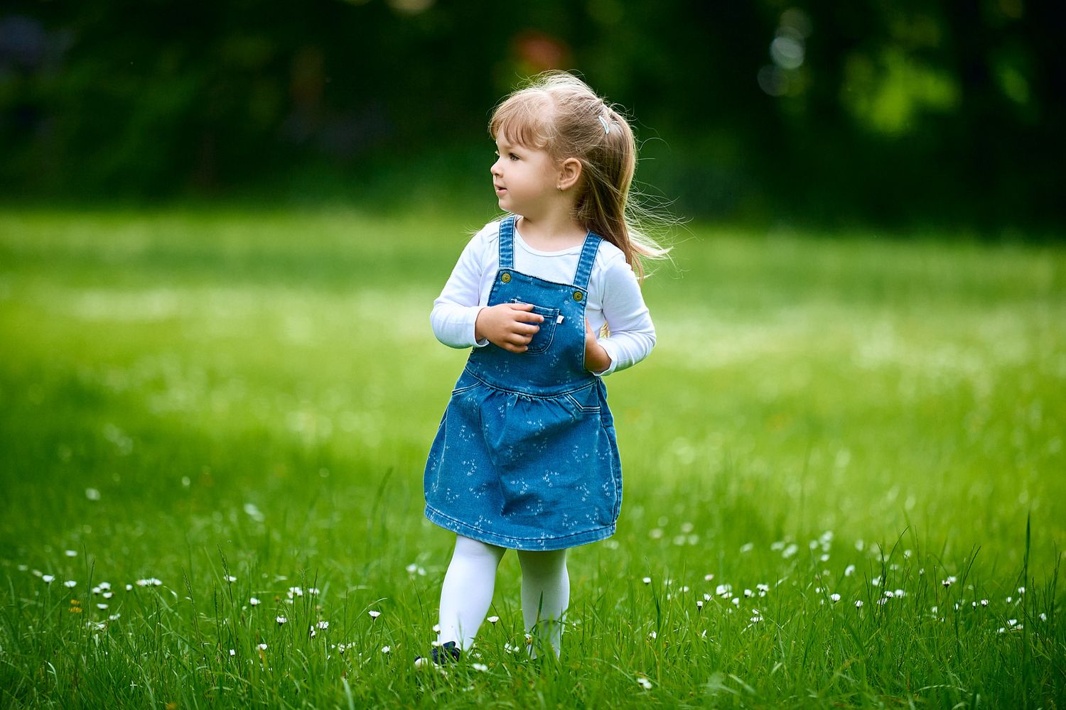 Small child in blue dress running through grassy field with white flowers.