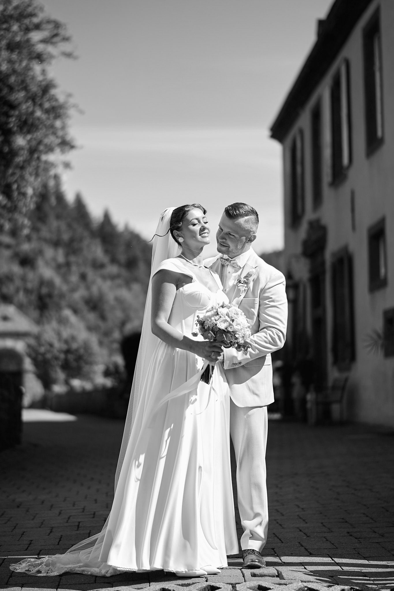 A romantic wedding photoshoot in black and white featuring a couple in white attire outdoors.