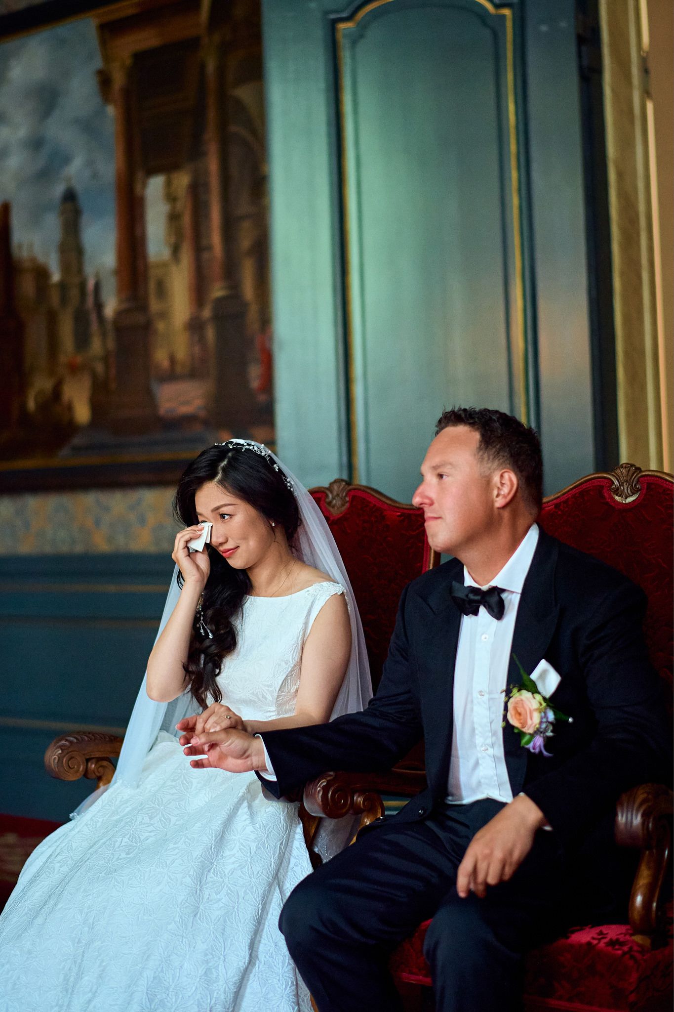 Newlyweds share intimate moments while resting on an elegant red couch in a formal setting.