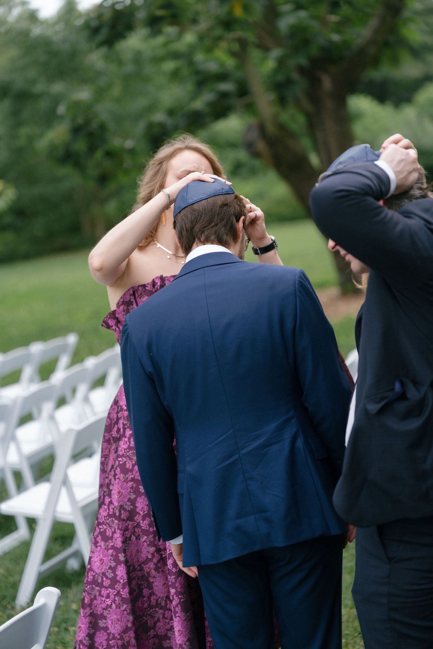 Woman placing a kippah on a groom's head at an outdoor Jewish wedding ceremony.