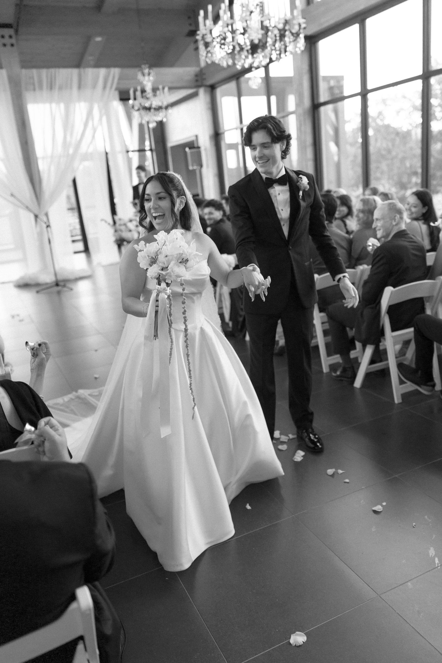 Bride and groom walk joyfully down aisle after wedding ceremony in elegant glass venue.