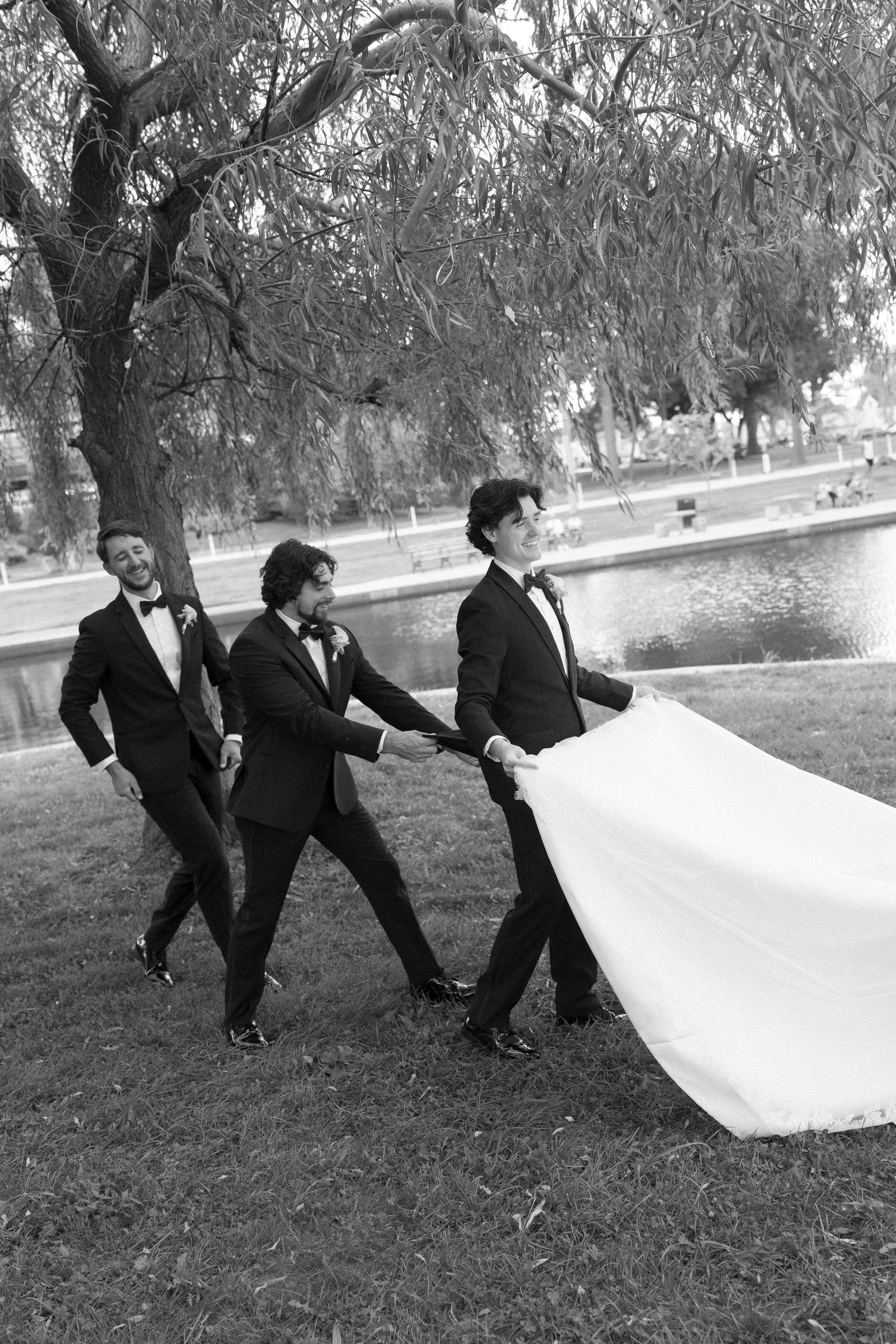 Groomsmen playfully carrying the bride's wedding dress train in black and white photo.