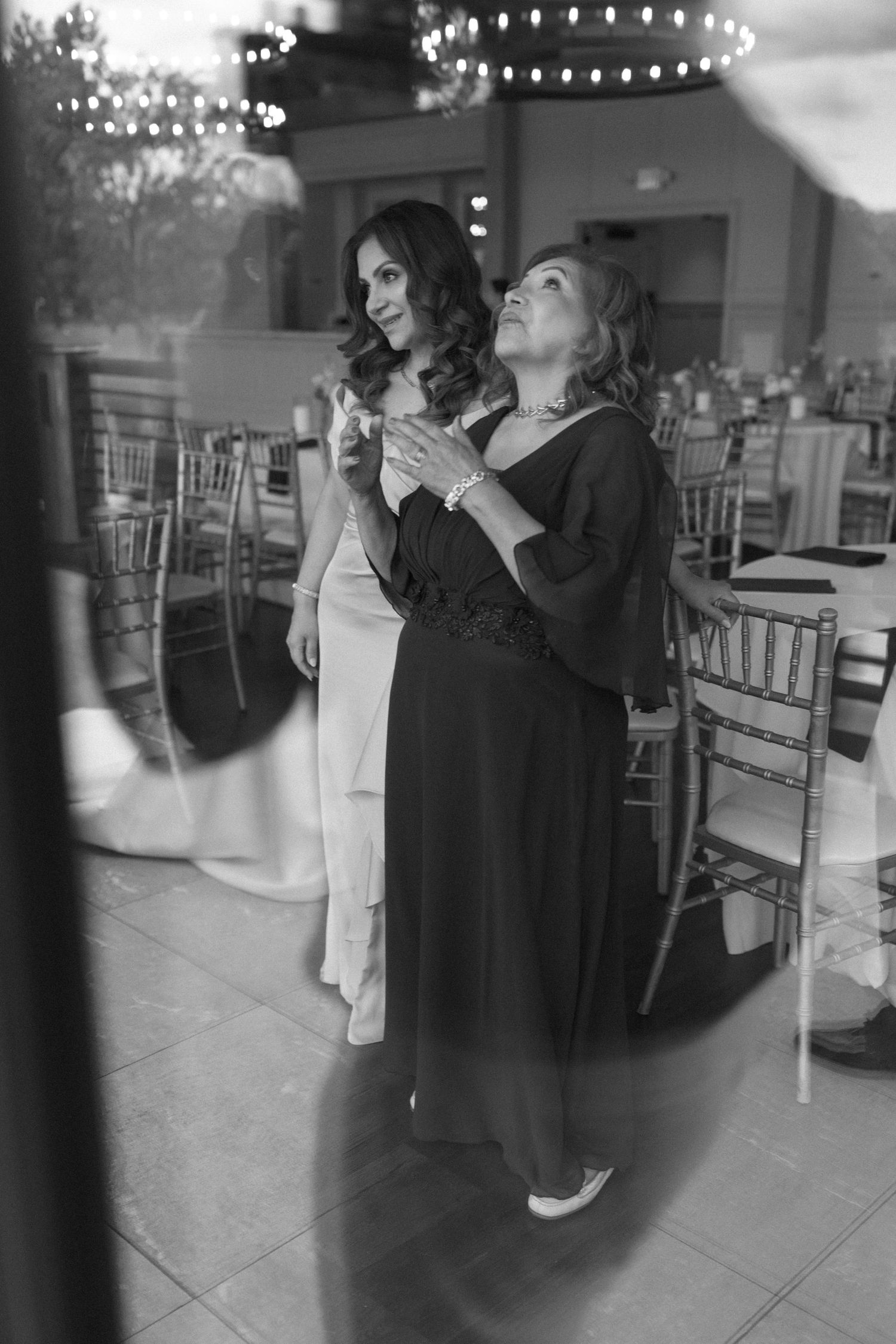 Black and white photo of bride and mother sharing an emotional moment in wedding venue.