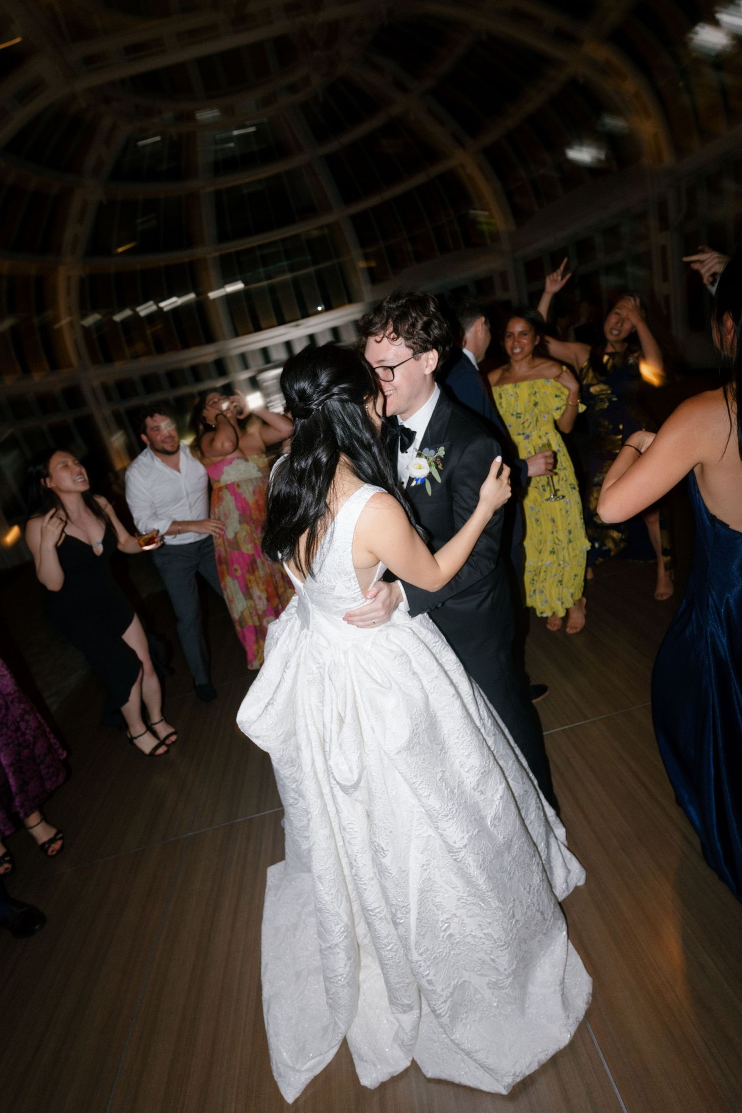 Bride and groom share a romantic kiss while dancing surrounded by guests at wedding reception.