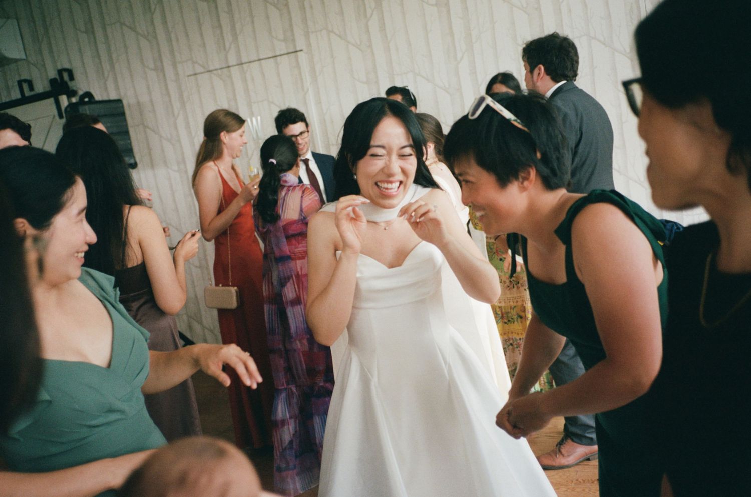 Joyful bride in white gown laughing with guests during wedding reception celebration.