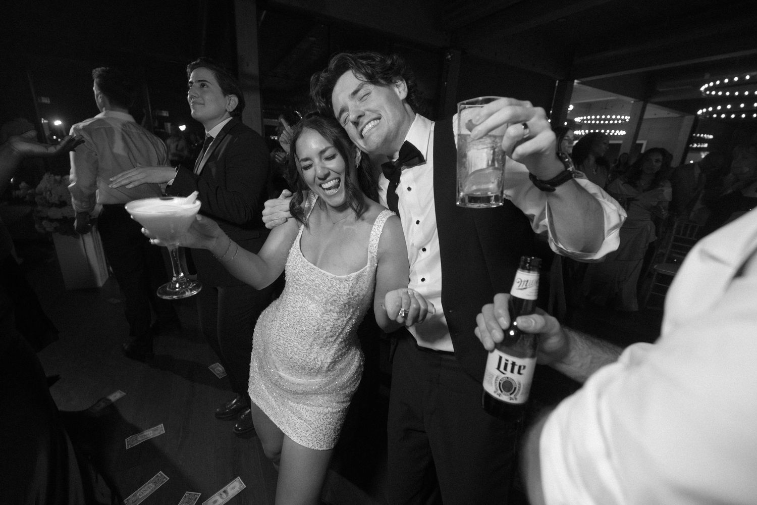 Black and white photo of bride and groom celebrating with drinks at wedding reception.