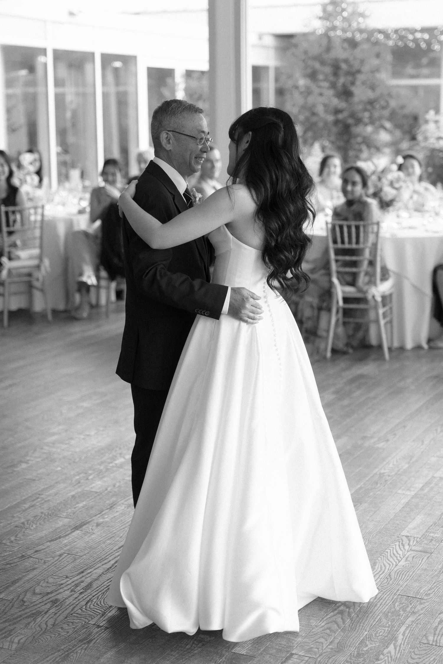 Black and white photo of bride and older man sharing a father-daughter dance at elegant wedding reception.