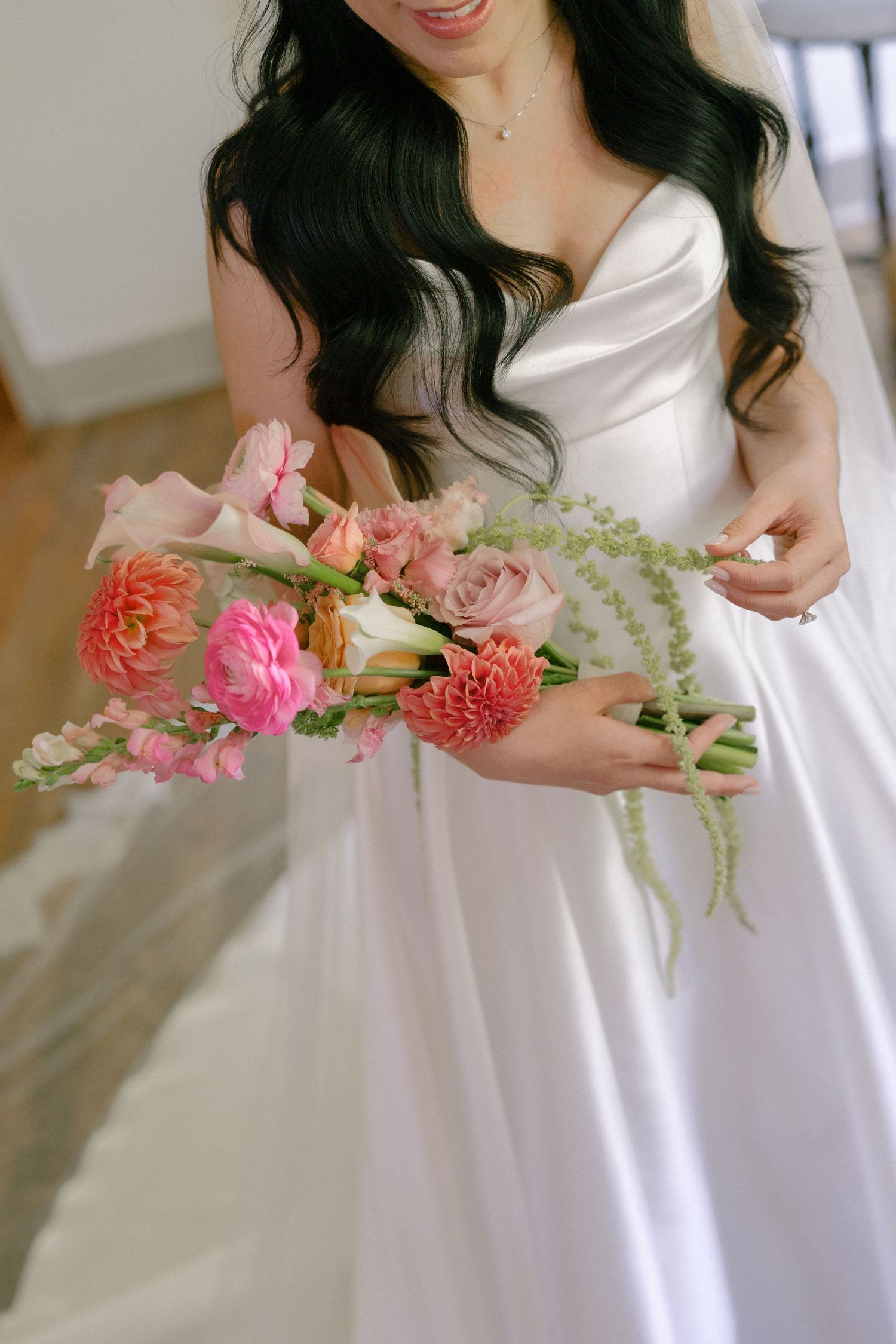 Bride in white satin gown holding a vibrant pink and coral wedding bouquet with roses and dahlias.
