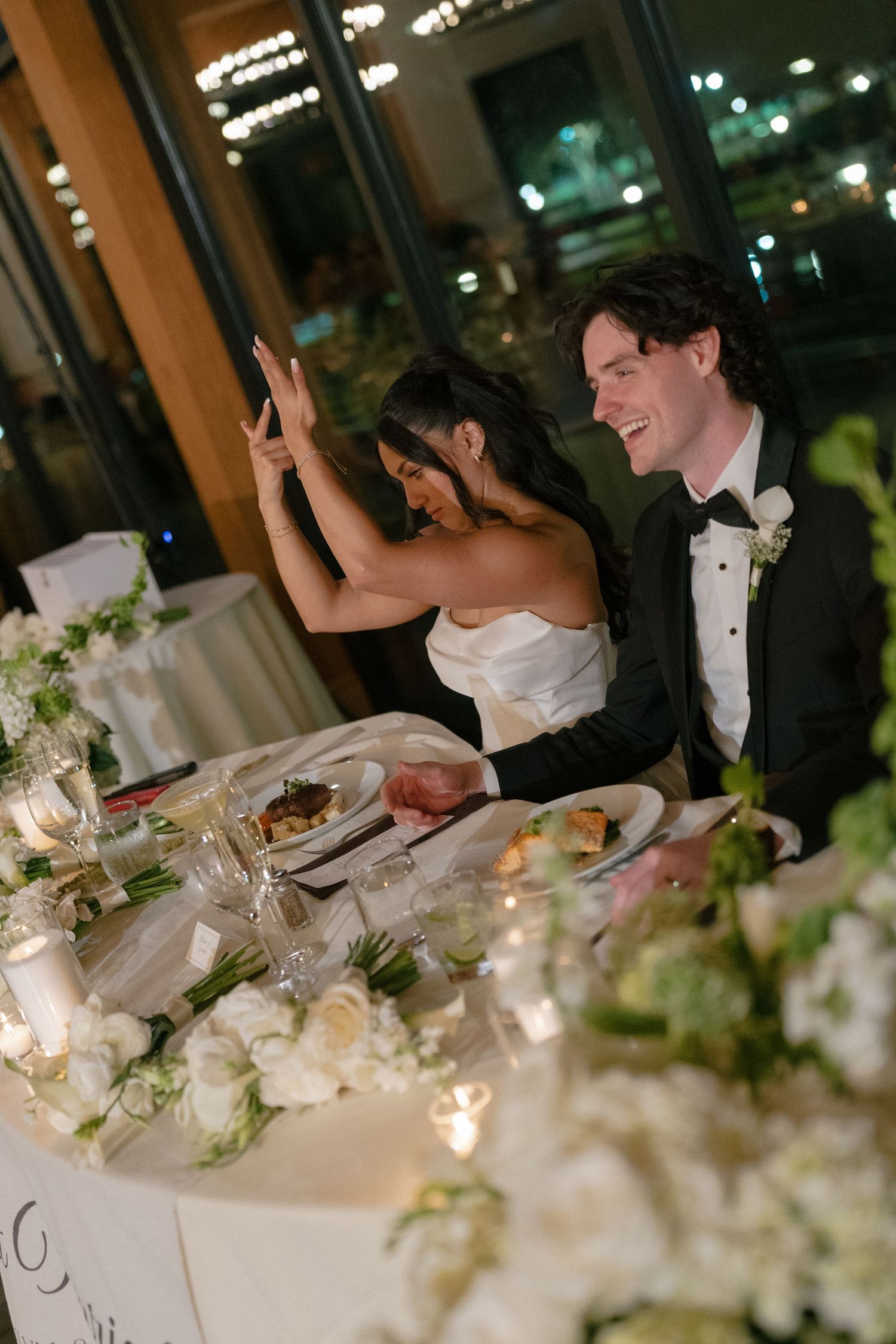 Bride and groom laughing together at sweetheart table with white floral centerpieces.