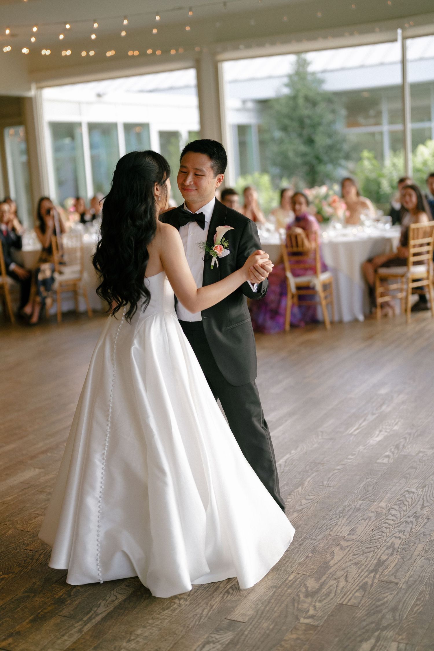 Bride and groom share intimate first dance in elegant reception hall with guests watching.