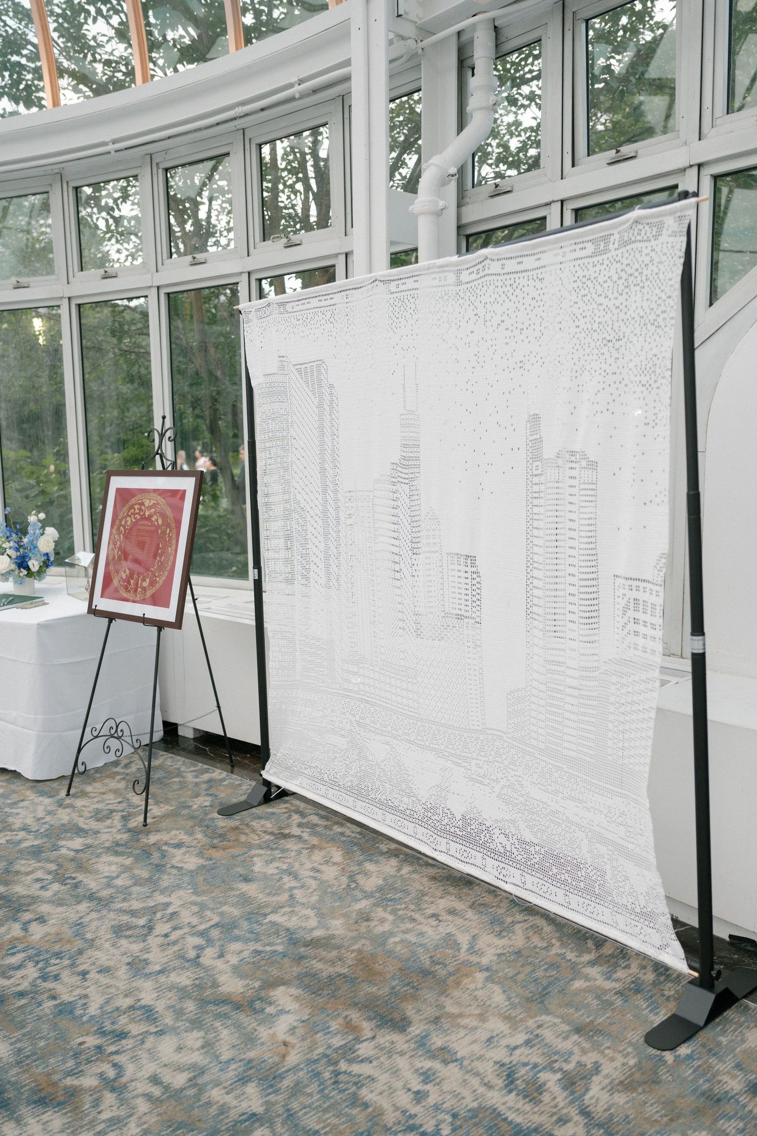 Wedding venue display featuring a detailed cityscape ketubah backdrop and framed artwork on an easel.