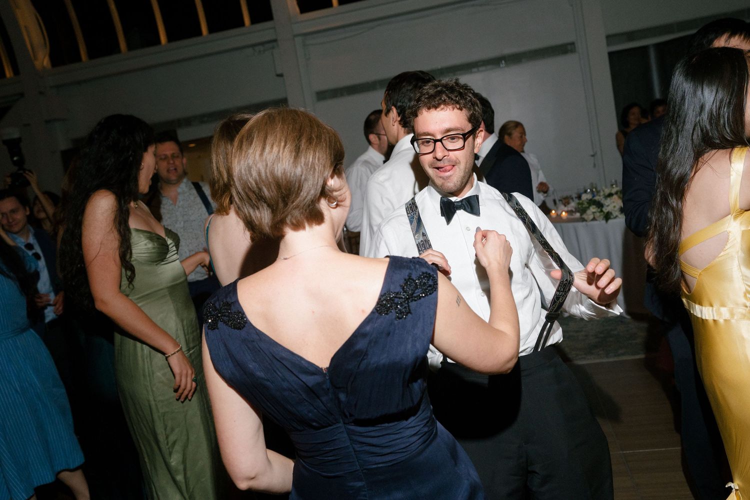 Couple dancing together at a wedding reception, man in suspenders and bow tie, woman in navy blue dress.